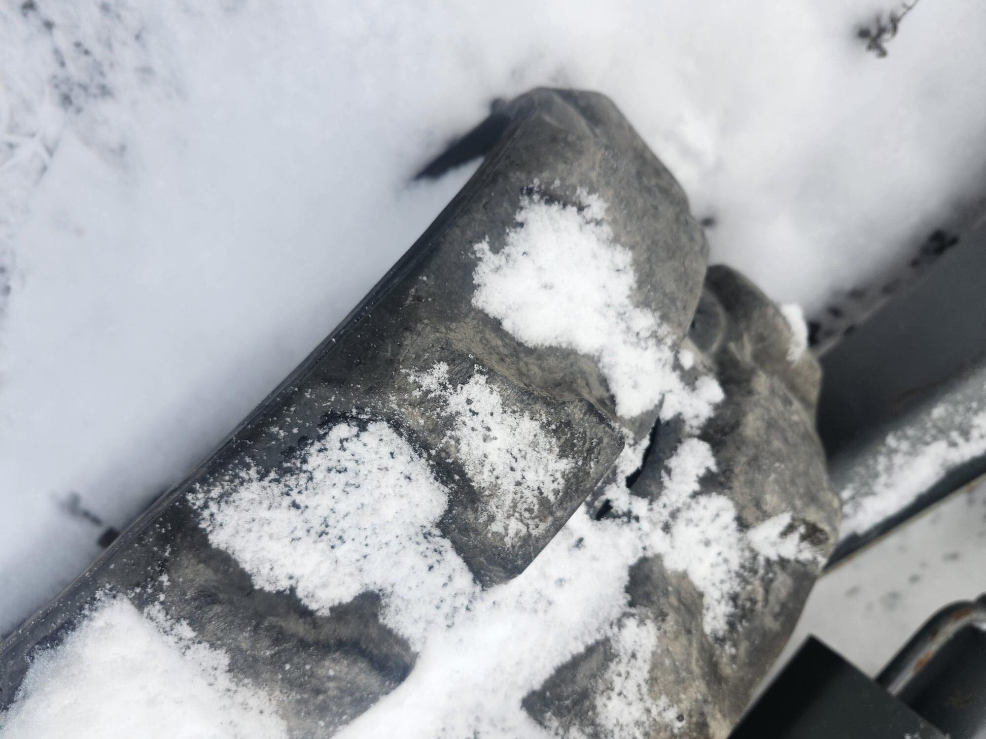 Une pierre patinée, partiellement recouverte de neige, entourée de neige. La texture de la pierre est rugueuse et la neige blanche crée un contraste avec la surface plus sombre de la pierre.