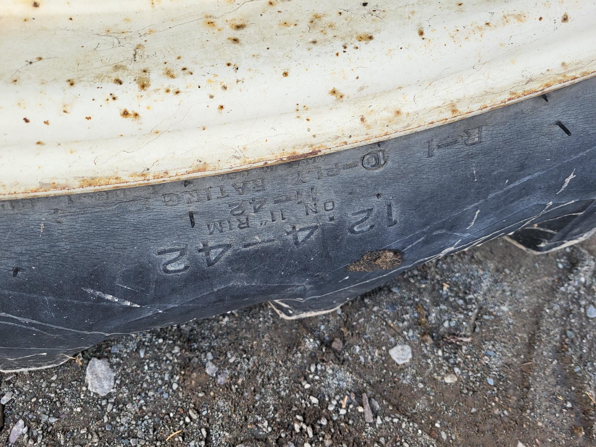 Close-up of a tire appears to be partially buried in dirt. The tire's sidewall is visible, showing the size 