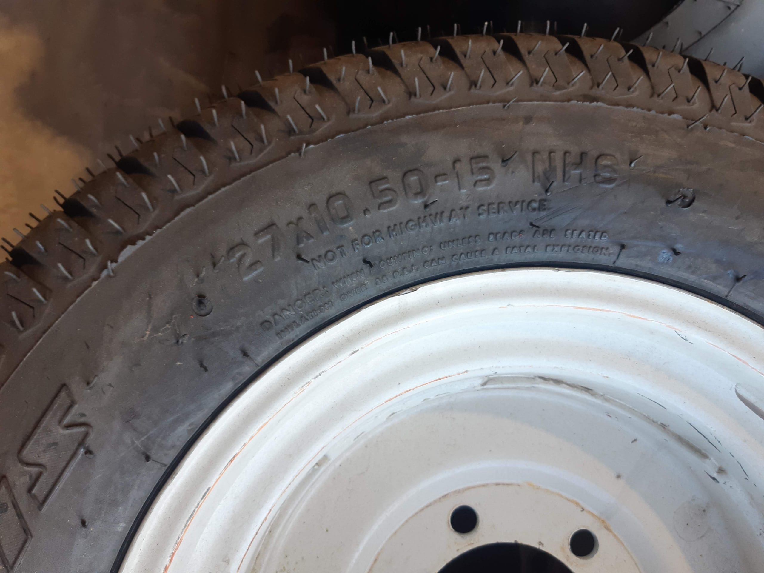 A close-up image of a tire mounted on a white wheel rim. The tire features a knobby tread pattern and has text on its sidewall reading 