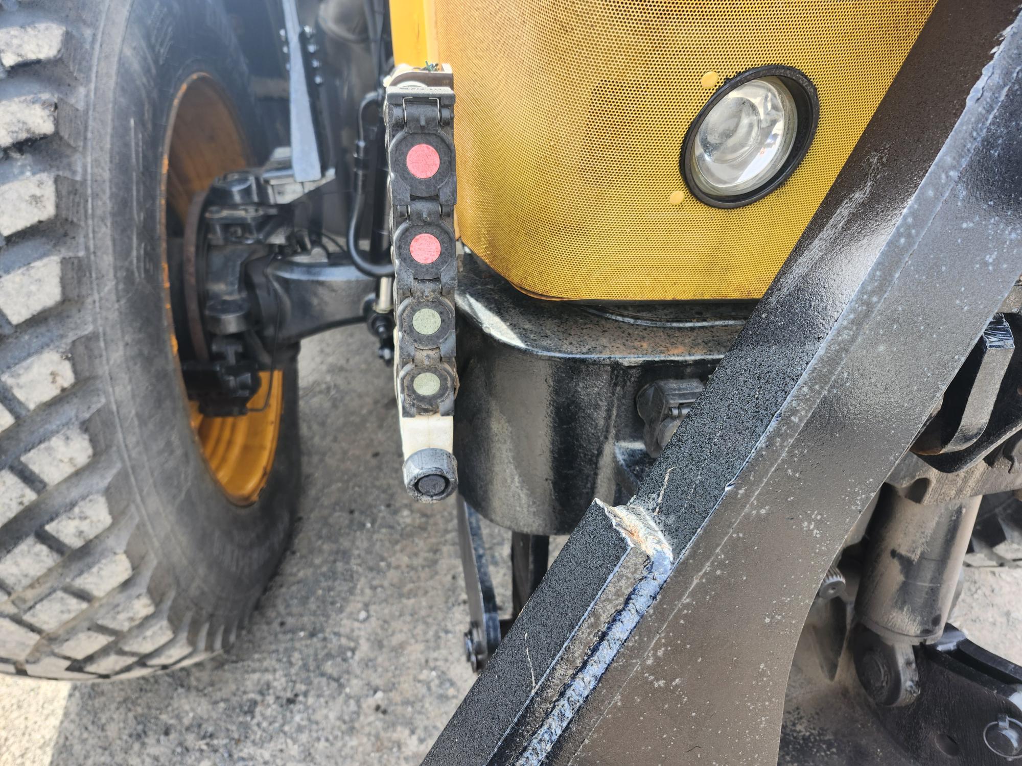 Gros plan d'un véhicule de construction jaune montrant son gros pneu, une partie de l'attache avant, un phare rond et une bande verticale avec des feux indicateurs colorés.
