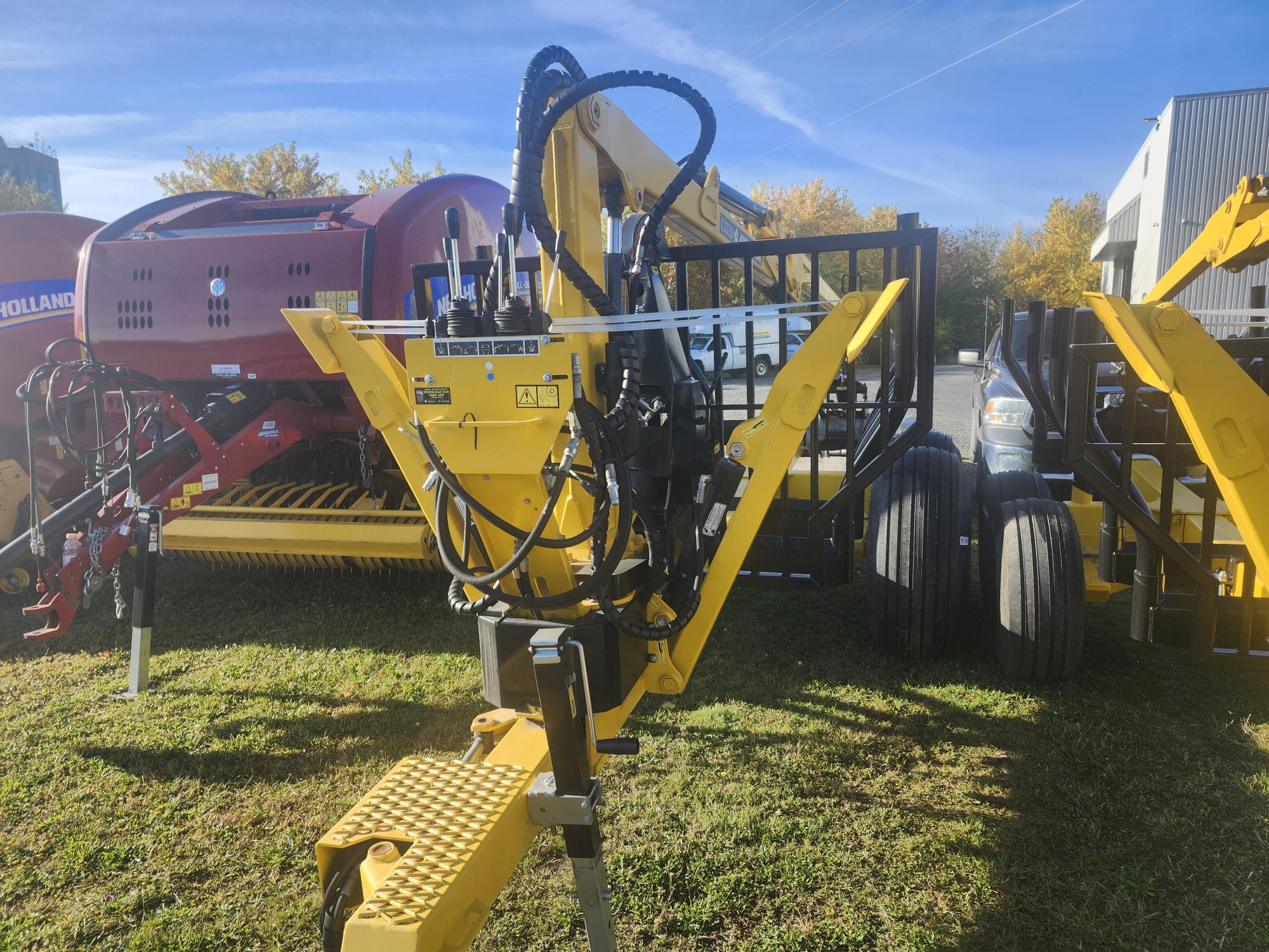 Machines agricoles exposées dans un espace vert, avec un équipement jaune et noir équipé de divers systèmes hydrauliques et commandes. D'autres machines sont visibles en arrière-plan, et des arbres au feuillage d'automne sont sous un ciel bleu.