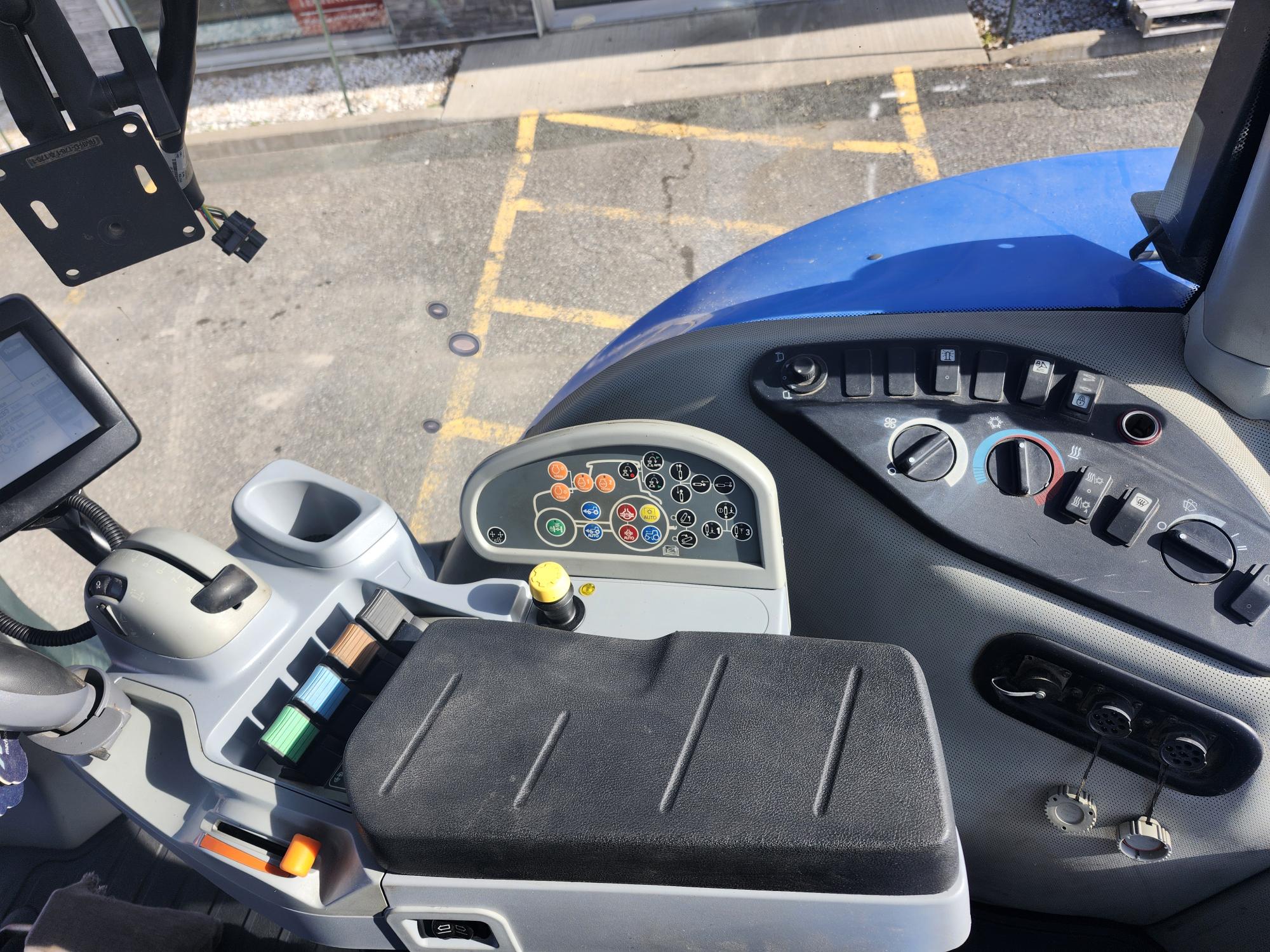 Vue intérieure du tableau de bord d'un véhicule, montrant diverses commandes et boutons. Le panneau comprend un volant, des leviers et un petit écran numérique. Le trottoir extérieur est visible à travers la fenêtre.