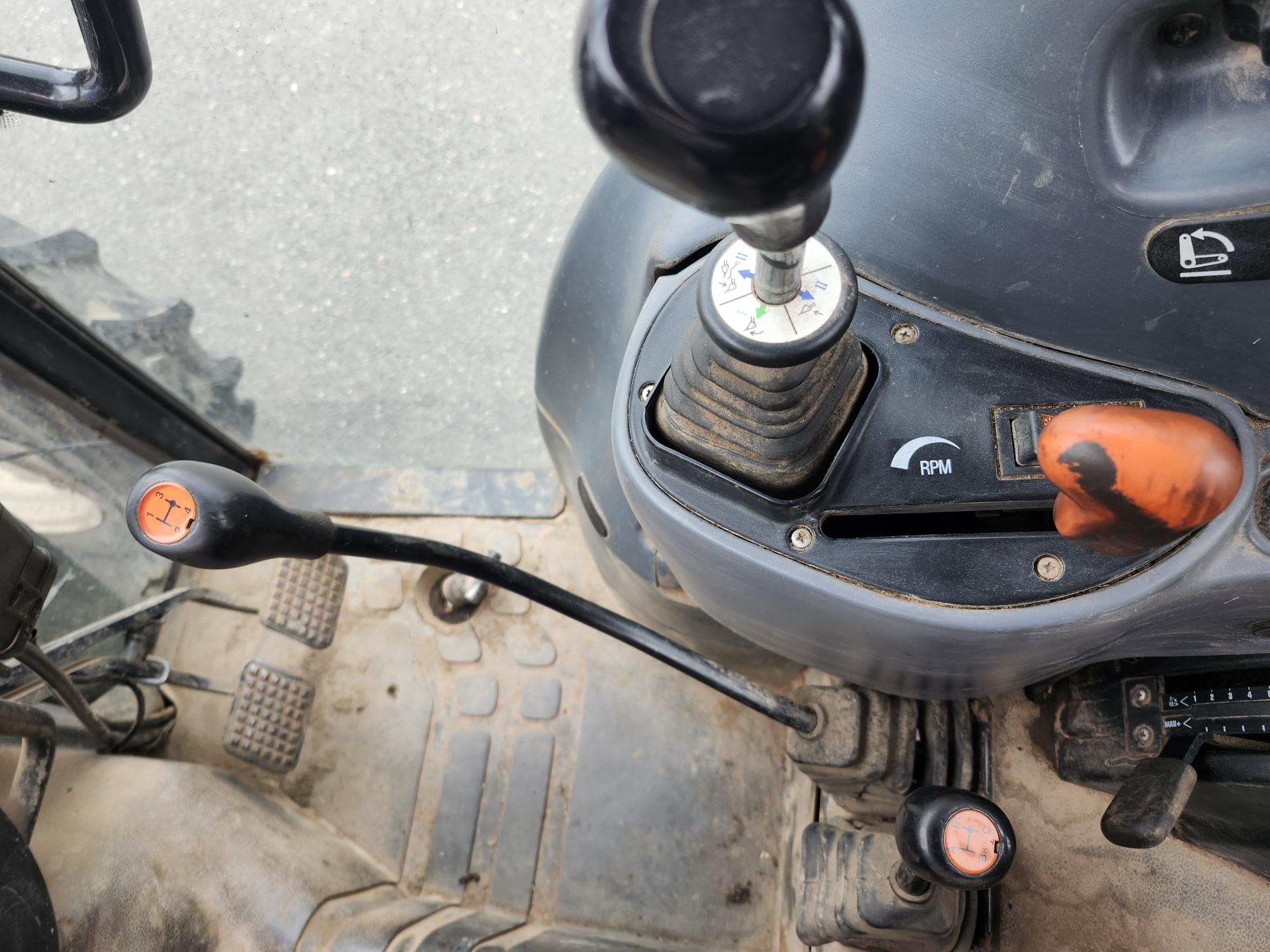 Gros plan de l'intérieur d'un tracteur montrant les leviers de vitesses, le cadran de régime et les pédales. Le tableau de bord est poussiéreux et les commandes sont bien utilisées. La vue est du point de vue du conducteur, se concentrant sur les commandes opérationnelles.