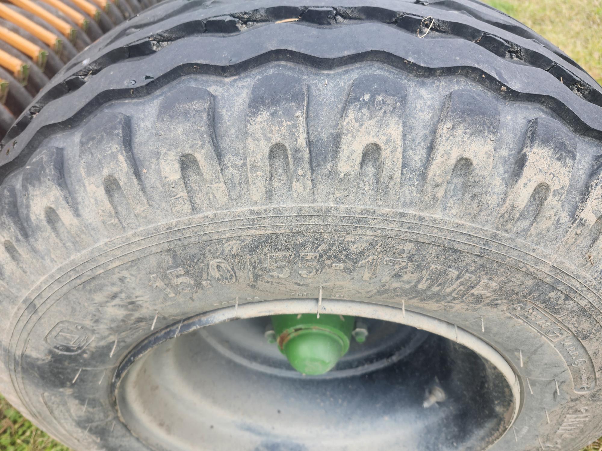 Gros plan d'un pneu en caoutchouc noir usé avec des bandes de roulement visibles et un moyeu vert. Le pneu est monté sur une jante métallique et semble faire partie d'un équipement d'extérieur, placé sur l'herbe. Le texte sur le pneu indique « 4.00-8 » et d'autres spécifications.