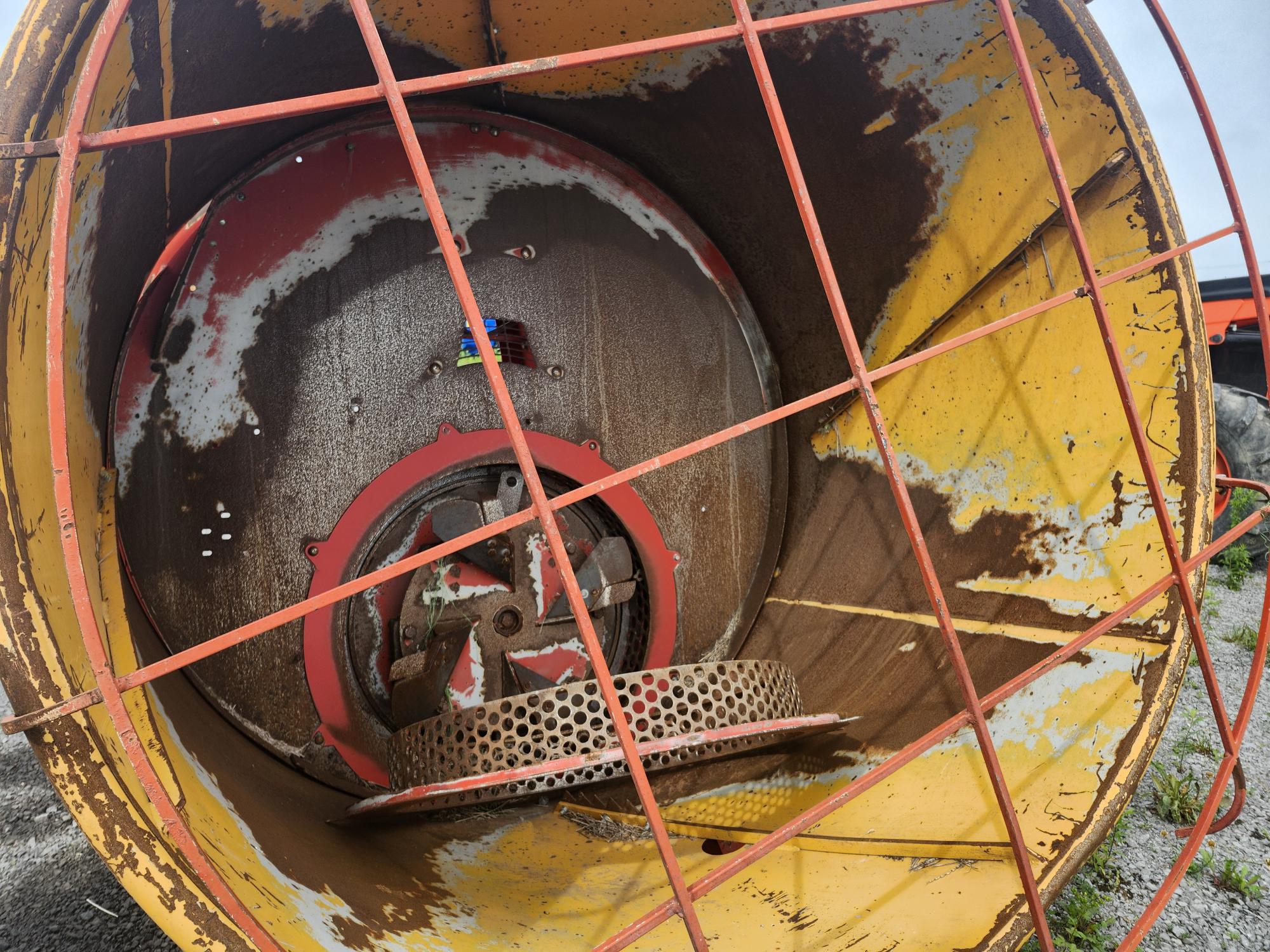 Gros plan de l'intérieur d'un grand tambour ou cylindre industriel usé par les intempéries, avec de la peinture écaillée et de la rouille. Le tambour est entouré d'une structure métallique orange et une structure circulaire en forme d'éventail est visible à l'intérieur.