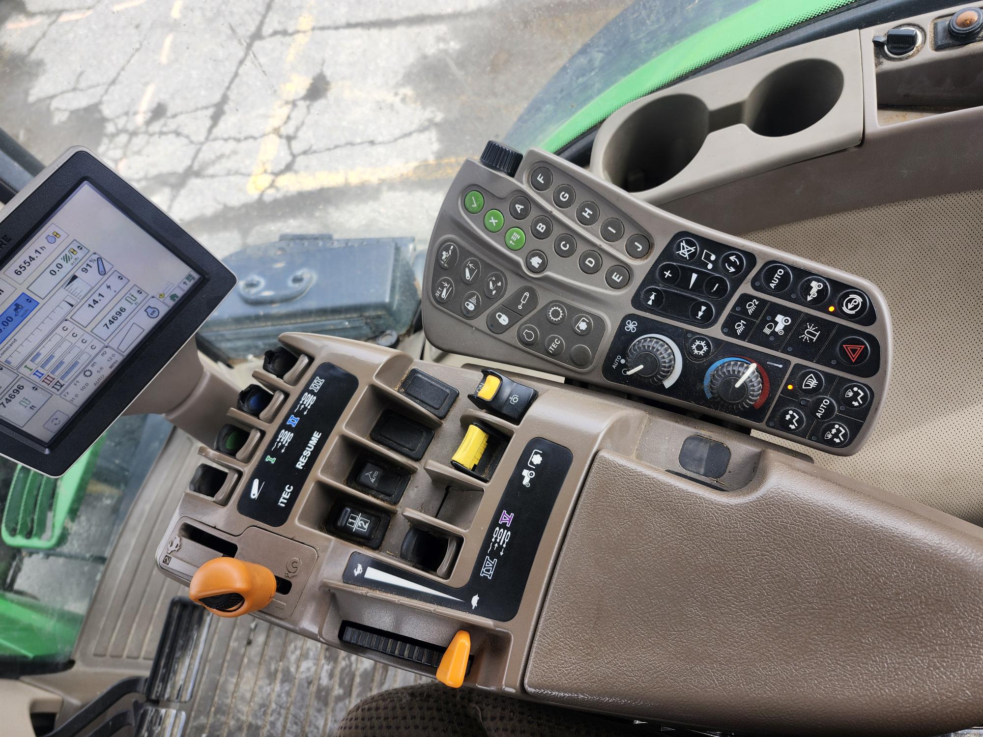 Panneau de commande et écran tactile à l'intérieur d'une cabine de tracteur moderne, montrant de nombreux boutons, interrupteurs, cadrans et leviers, avec une partie d'un siège et des porte-gobelets visibles.