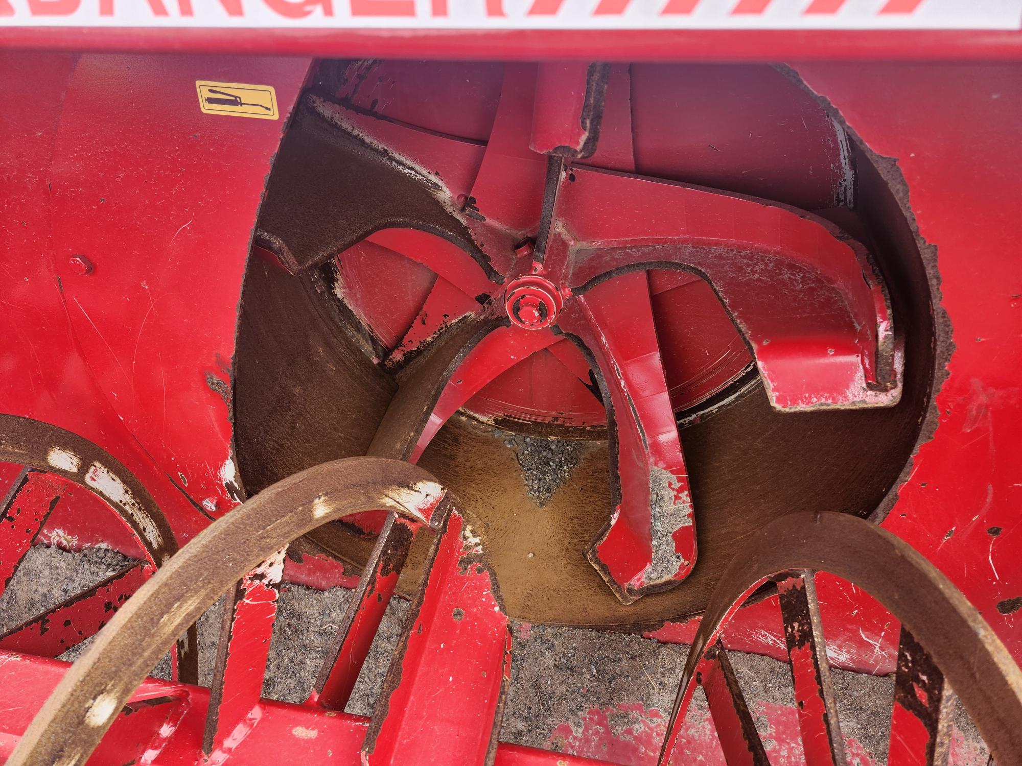 Vue rapprochée du mécanisme intérieur d'une machine agricole rouge, comportant des lames métalliques et des composants incurvés avec de la peinture usée et des traces de rouille.