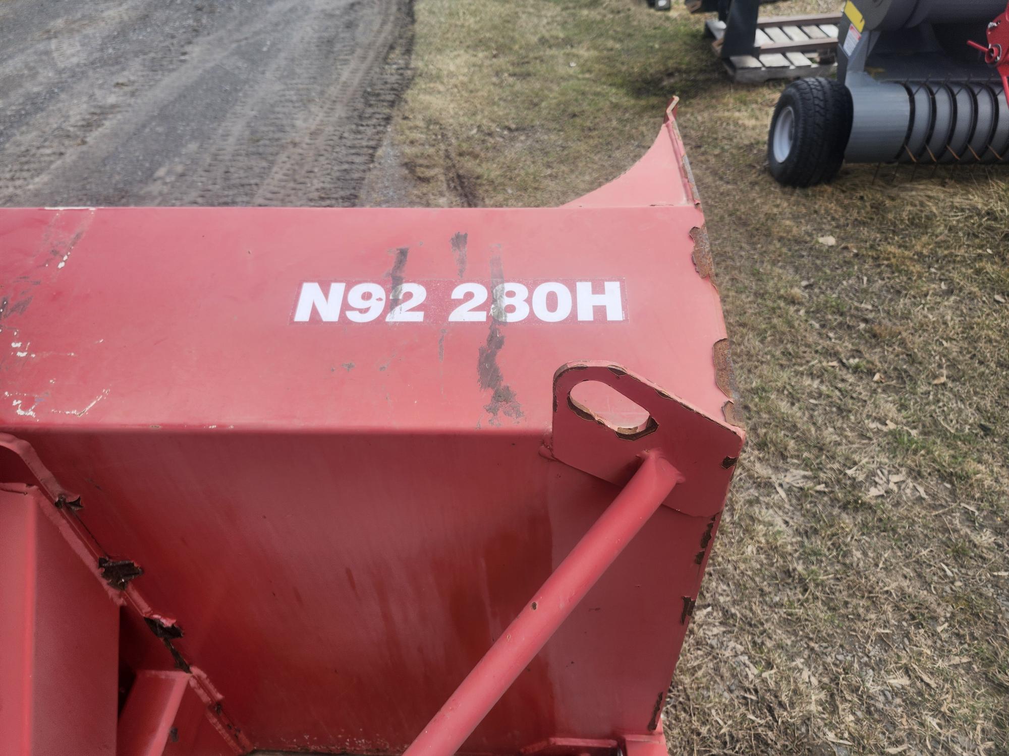 Gros plan d'une pièce de machine agricole en métal rouge avec l'étiquette « N92 230H » peinte en blanc sur sa surface ; le sol et d'autres équipements sont visibles en arrière-plan.