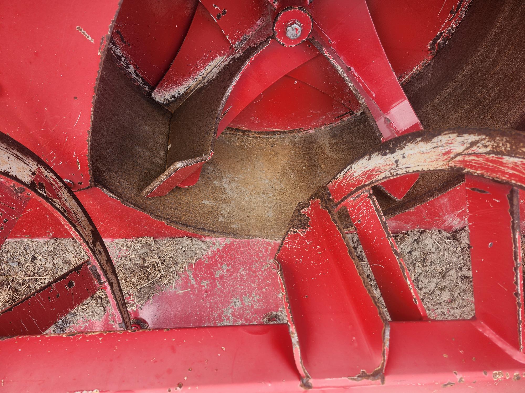 Gros plan de pièces métalliques rouges et usées et de lames à l'intérieur d'une machine agricole ou d'un mélangeur, avec des traces de saleté et de rouille visibles sur les surfaces.