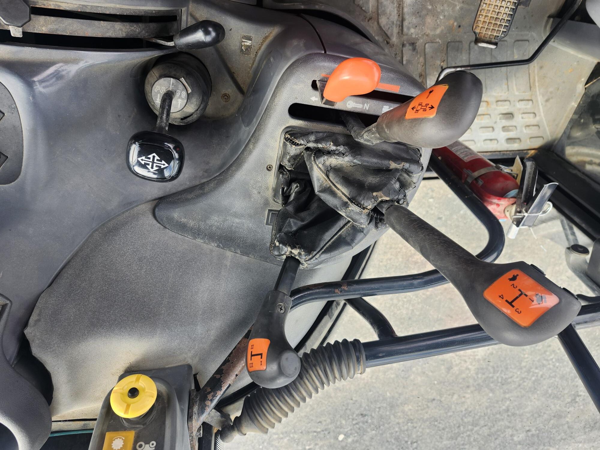 Gros plan du panneau de commande d'un tracteur montrant divers leviers et boutons, notamment l'allumage, le changement de vitesse et les commandes avec des poignées orange et jaunes comportant des symboles pour différentes fonctions du tracteur.