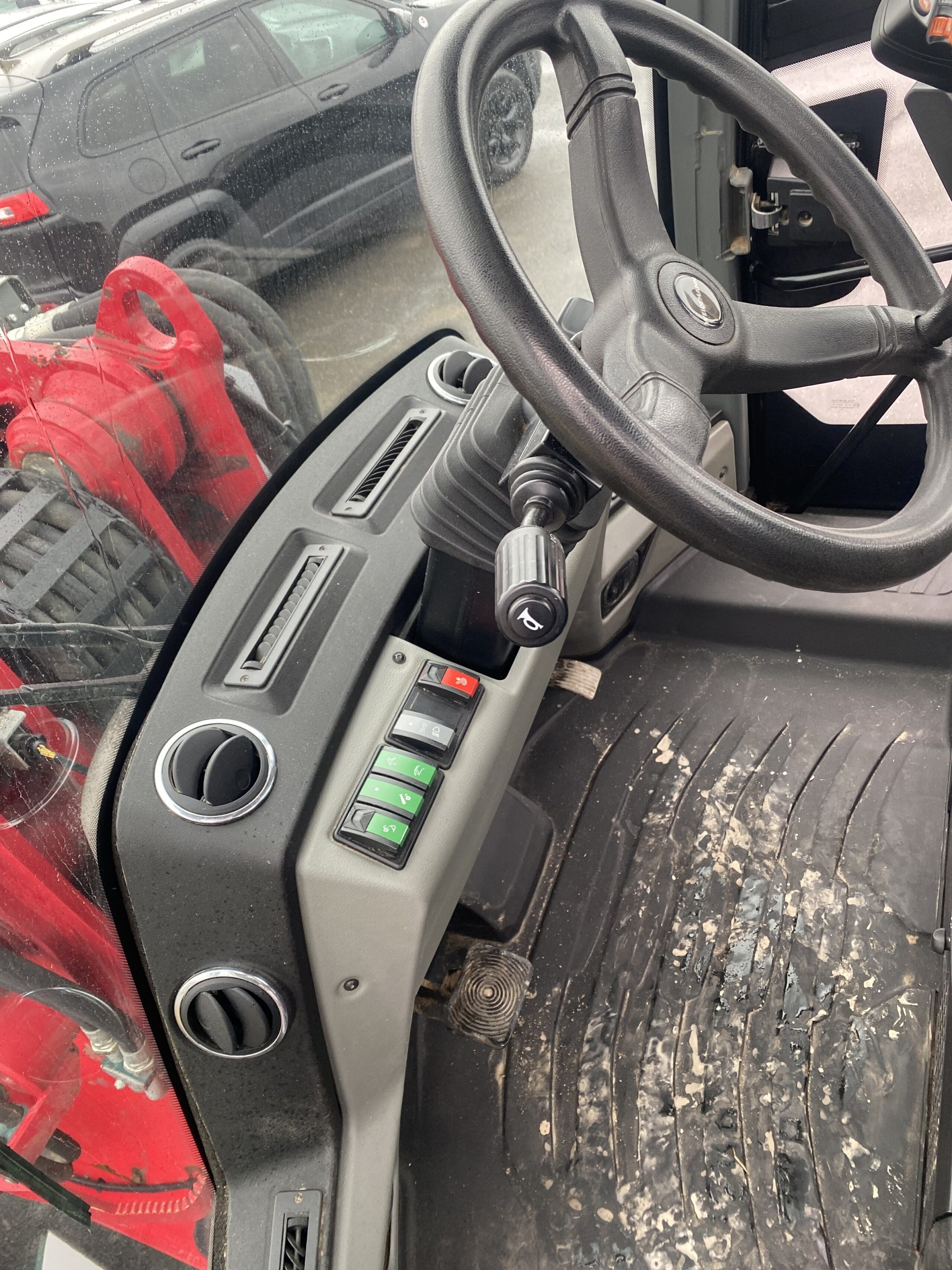 Gros plan de l'intérieur d'un véhicule montrant le volant, la clé de contact, les commandes du tableau de bord et un tapis de sol sale. Des machines rouges sont visibles à travers la vitre.