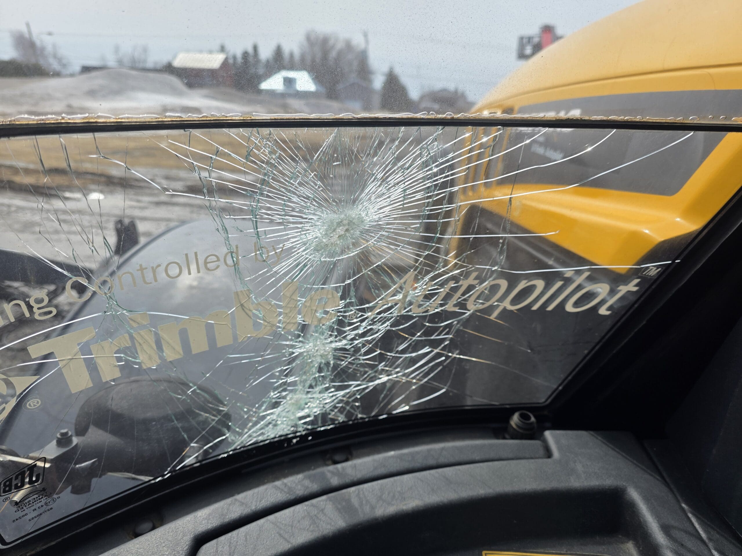 Un pare-brise fissuré avec un point d'impact important est vu de l'intérieur d'un véhicule. L'inscription « Trimble Autopilot » est partiellement visible, et un autobus scolaire jaune est visible à l'extérieur.