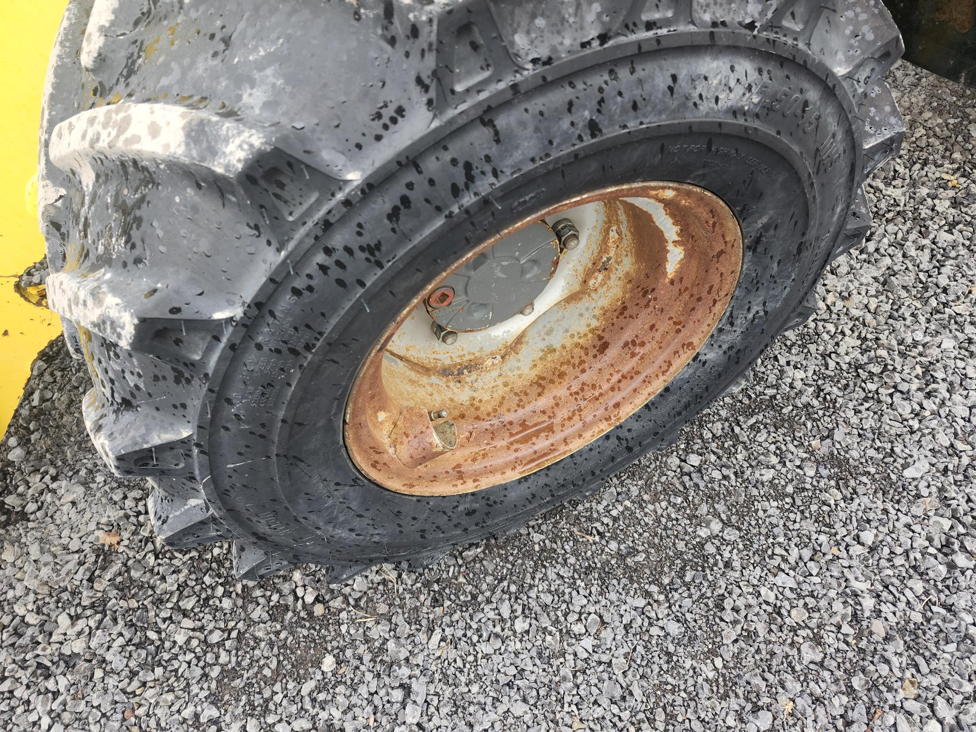 Gros plan d'un gros pneu de tracteur boueux avec une jante en métal rouillée, reposant sur une surface de gravier.