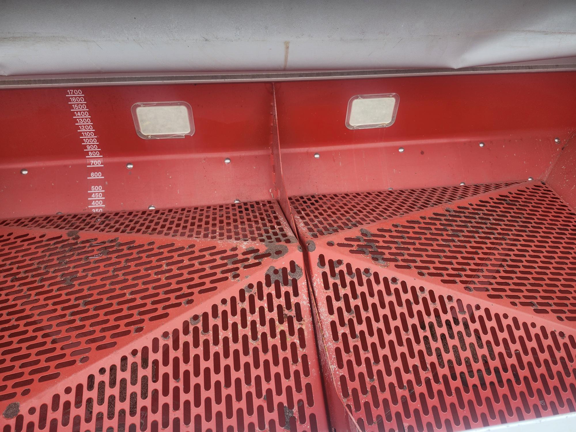 Poubelle métallique rouge à deux compartiments grillagés, graduée de 400 à 1700 sur la paroi gauche, et surmontée de deux petites fenêtres carrées. Des traces de saleté sont visibles sur les grilles.