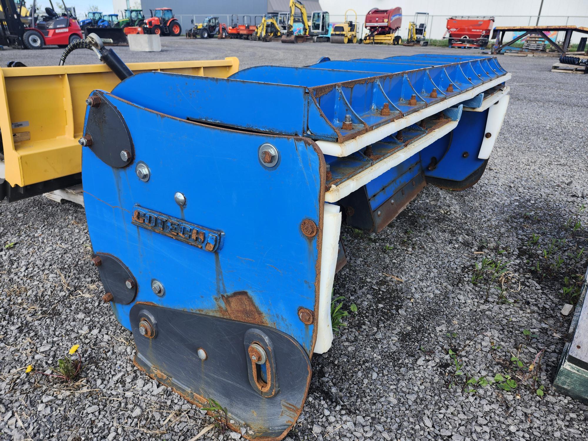 Une grande pièce de machine industrielle bleue et rouillée repose sur du gravier à l'extérieur, entourée d'autres machines et équipements dans une cour de stockage.
