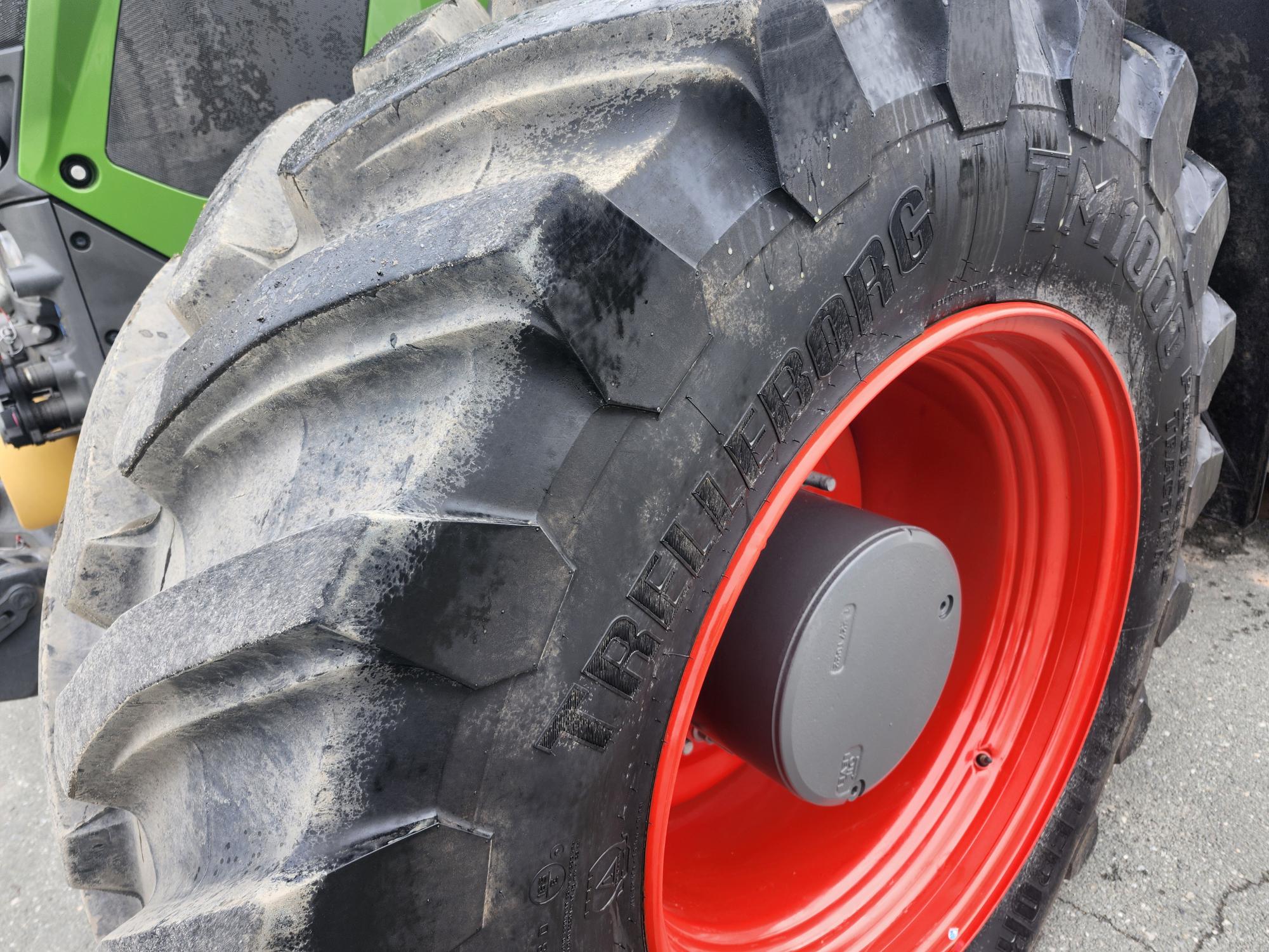 Gros plan d'un gros pneu de tracteur aux sculptures prononcées, maculé de boue. Le pneu est monté sur une jante rouge vif, et la marque « Trelleborg » est visible sur son flanc.