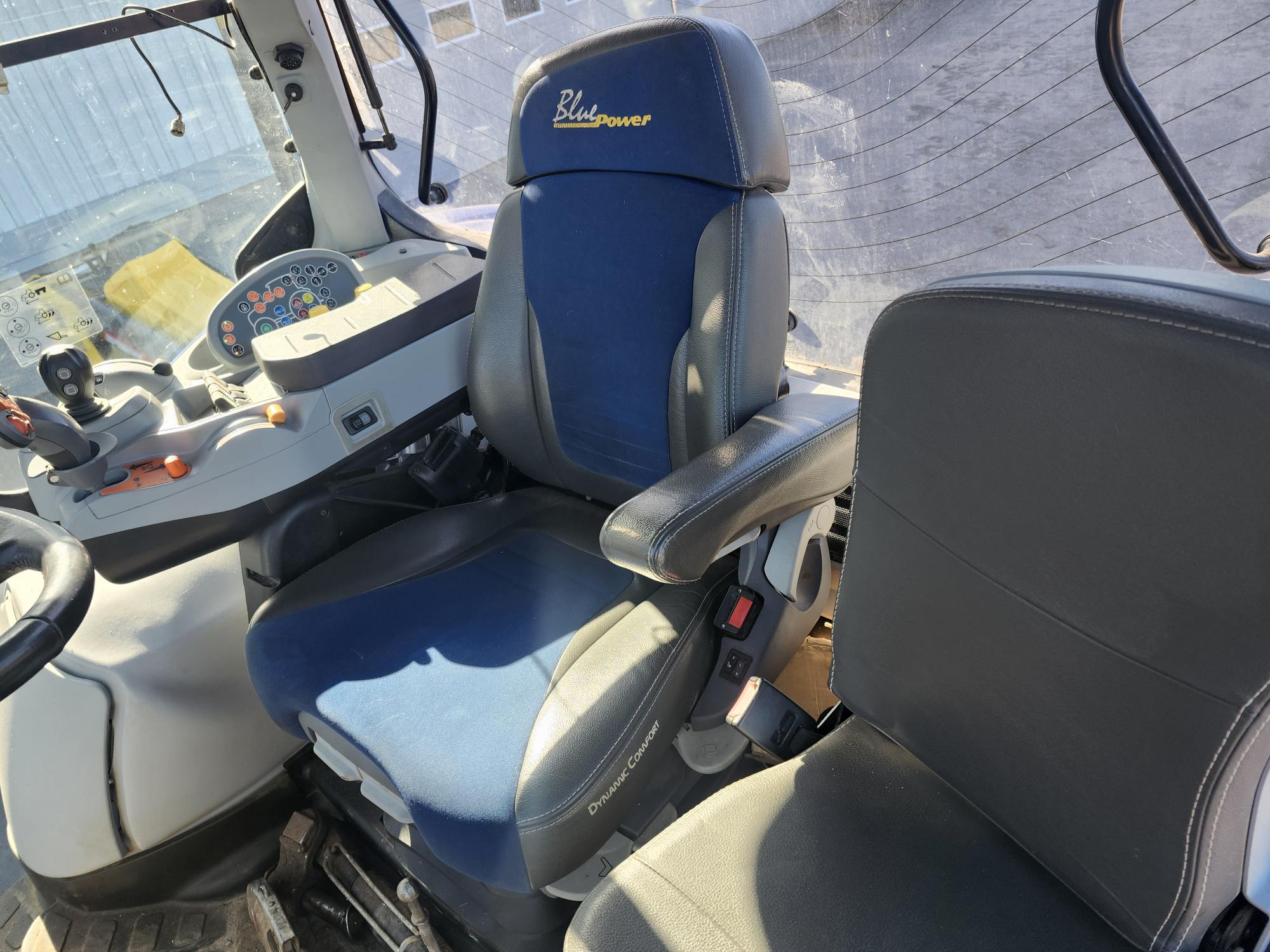 L'intérieur d'un véhicule, probablement un tracteur, montrant deux sièges - un bleu et gris avec « Blue Power » brodé sur l'appui-tête, et un noir - ainsi qu'un panneau de commande avec divers boutons et un volant.