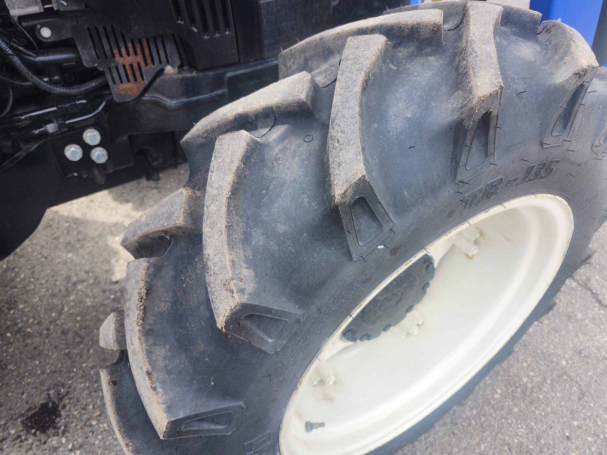 Gros plan d'un gros pneu de tracteur à bandes de roulement profondes et à jante blanche, monté sur un équipement agricole, sur une surface pavée.