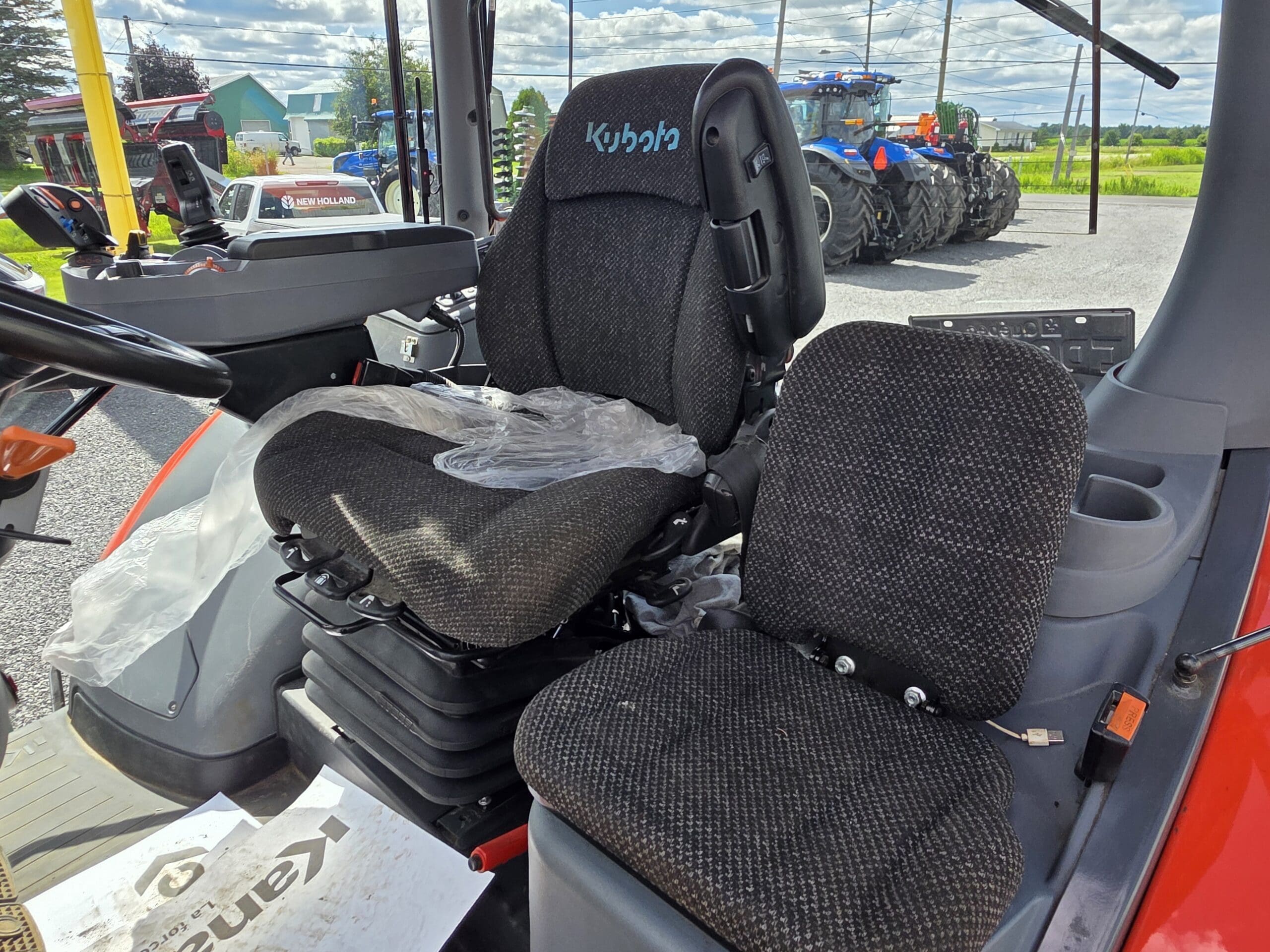 Intérieur d'une cabine de tracteur Kubota montrant deux sièges noirs rembourrés - un grand avec l'inscription 