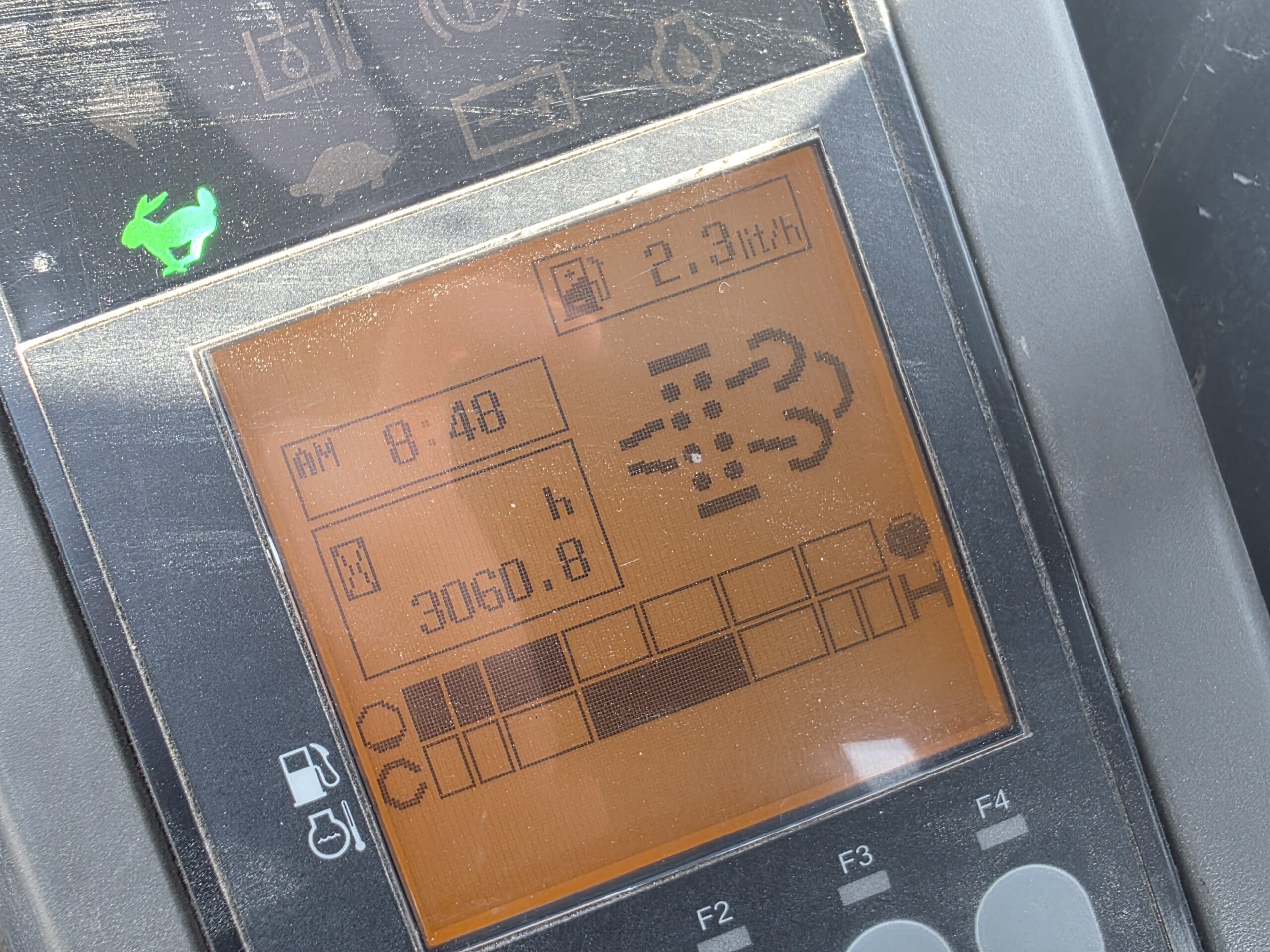 Gros plan d'un écran numérique orange affichant des informations sur le tableau de bord du tracteur : vitesse (2,3 mi/h), heure (8:48 AM), heures (3060,8 h), icônes de carburant et de moteur, et une icône verte de cerf dans le coin supérieur gauche.