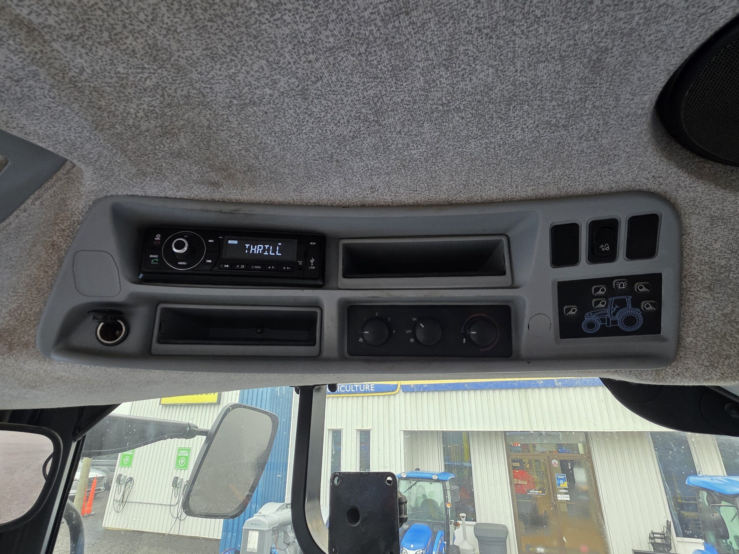 L'image montre le tableau de commande supérieur d'une cabine de véhicule, avec un écran radio indiquant 