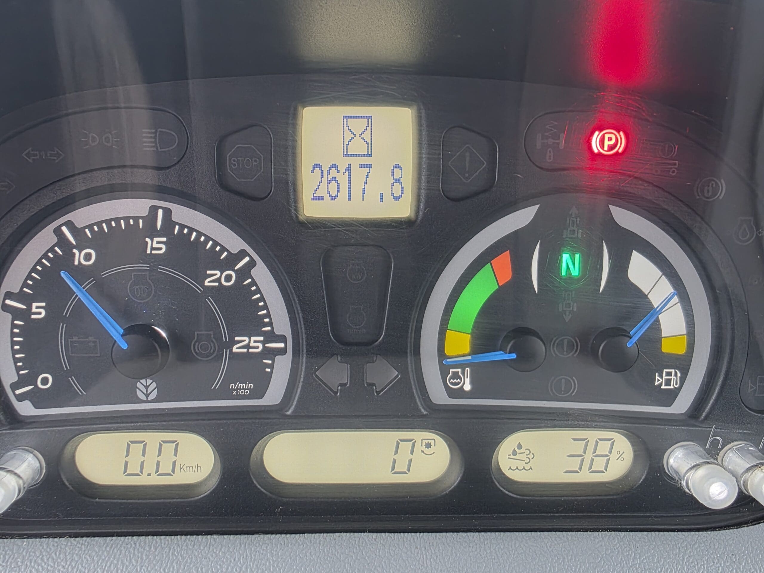 Gros plan du tableau de bord d'un véhicule montrant des jauges, des voyants d'avertissement et des affichages numériques, notamment un compteur de vitesse, un tachymètre, une jauge de carburant, 2617,8 heures, 0 km/h, 0°C et des indicateurs de 38 %, avec plusieurs voyants d'avertissement allumés.