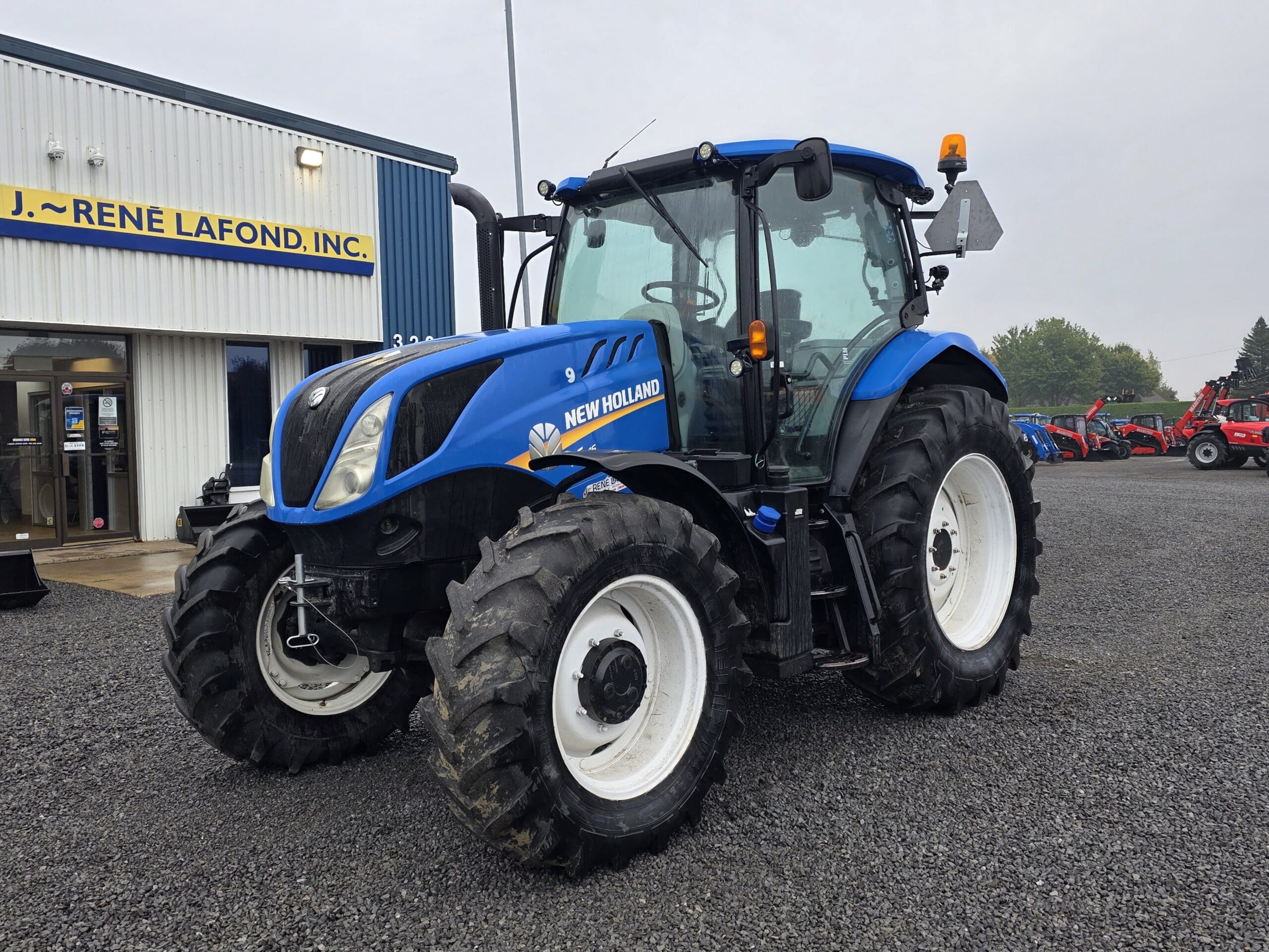 Un tracteur New Holland bleu est garé à l'extérieur d'un bâtiment sur lequel on peut lire 