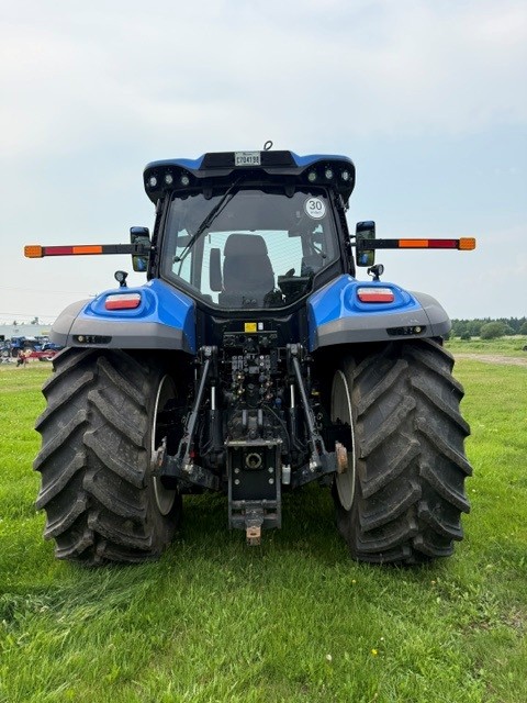 Vue arrière d'un tracteur bleu équipé de gros pneus noirs, garé sur de l'herbe verte, photographié en extérieur par temps nuageux.