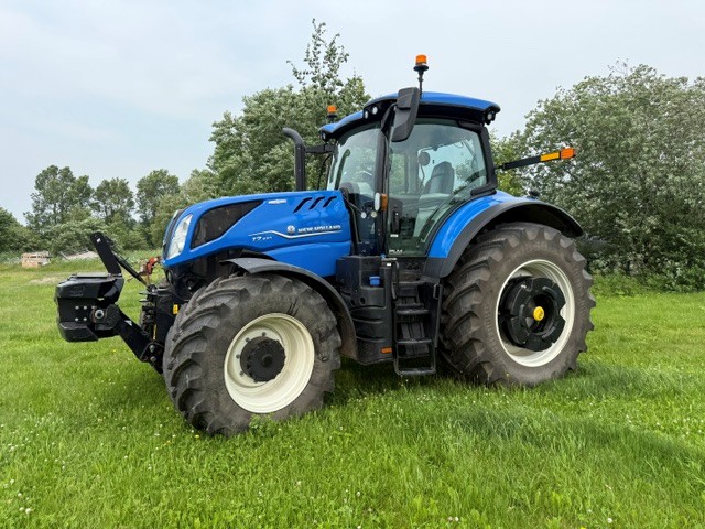 Un tracteur New Holland bleu est garé sur une pelouse verte, avec des arbres en arrière-plan, par une journée nuageuse.