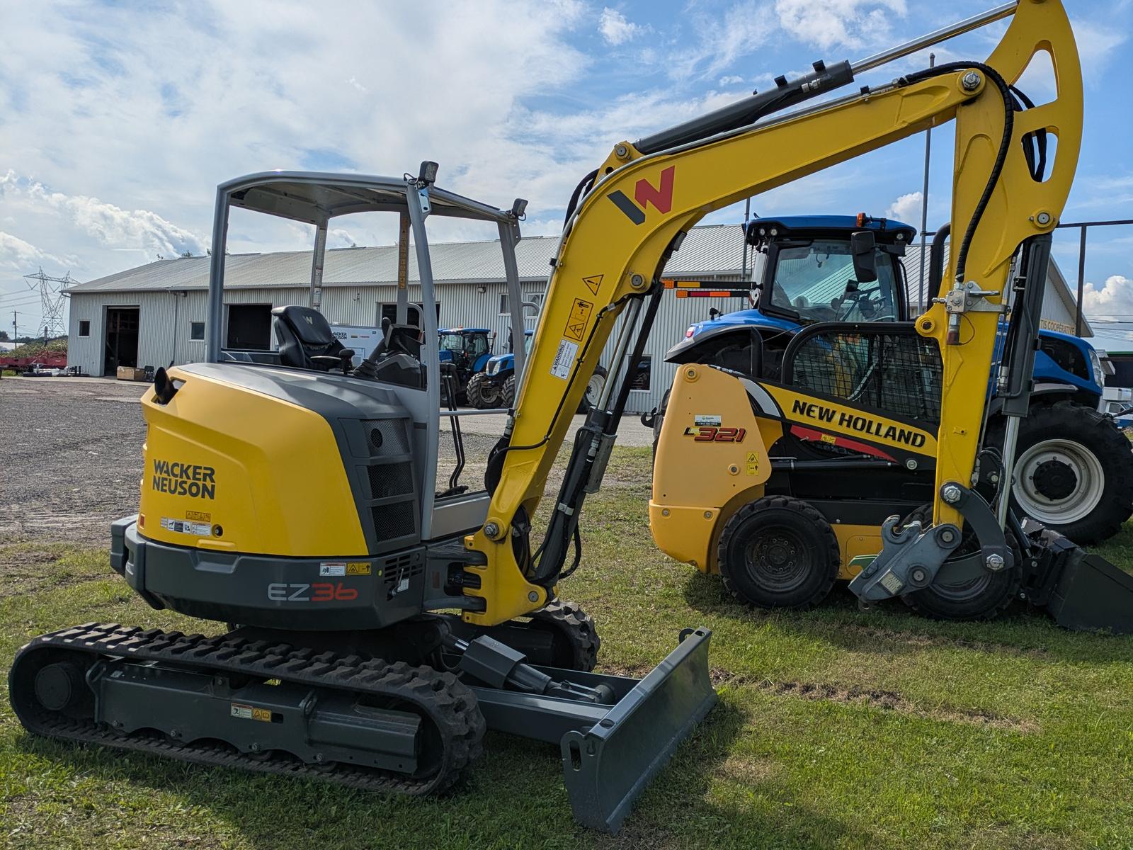Wacker Neuson EZ36 vu de trois quarts arrière, godet abaissé, bâtiment blanc en arrière-plan