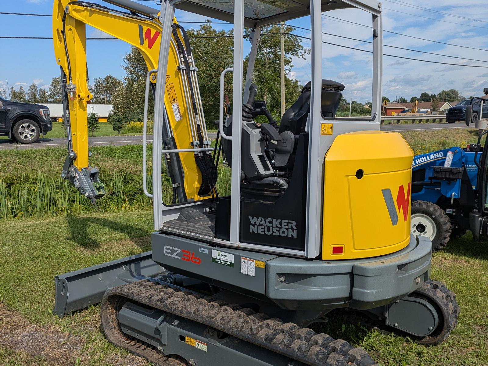 Wacker Neuson EZ36 vu de trois quarts arrière, bras articulé replié, cabine ouverte, stationnée sur le gazon