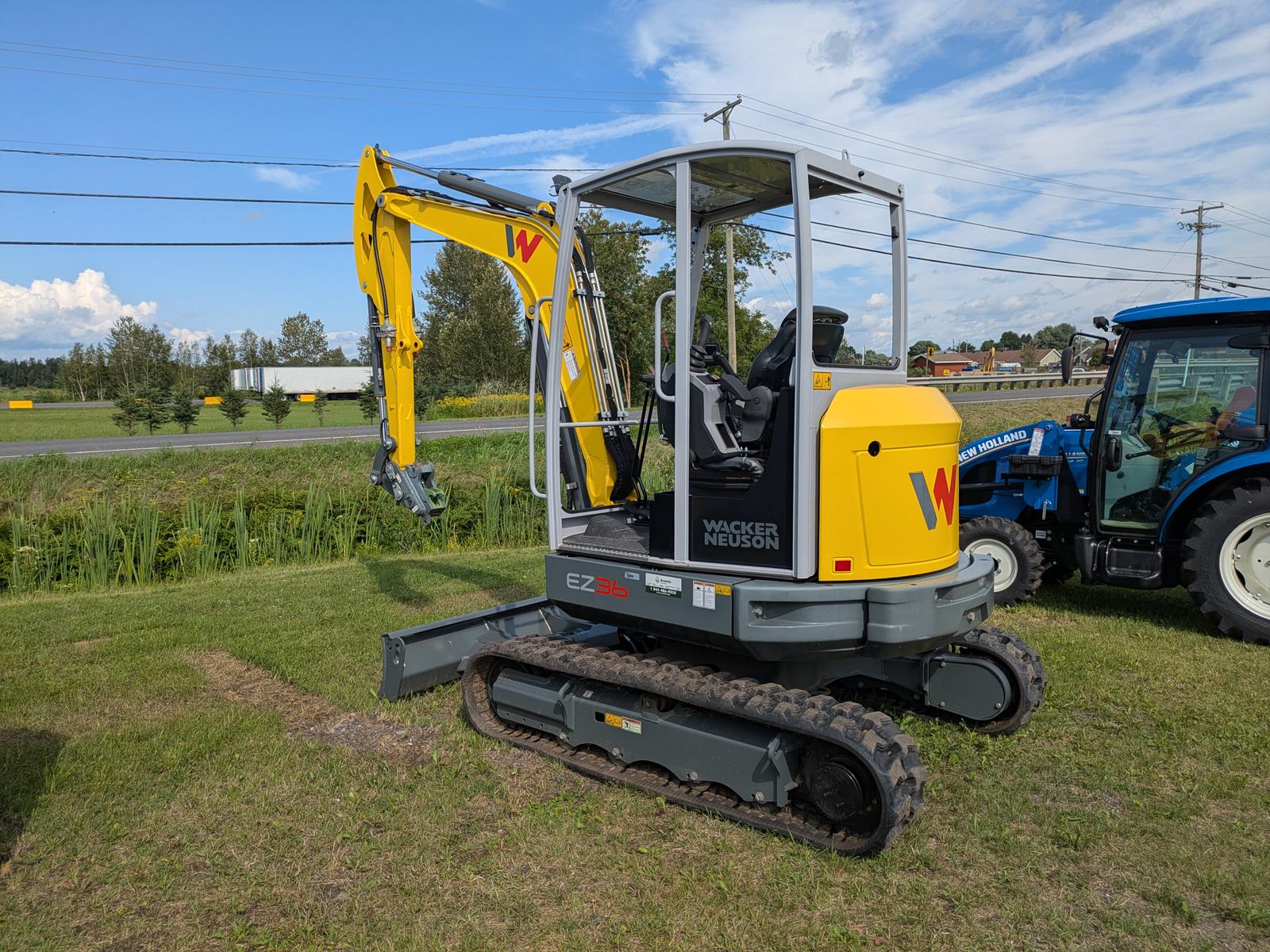 Wacker Neuson EZ36 vu de trois quarts avant-gauche, bras articulé relevé, autre machine en arrière-plan