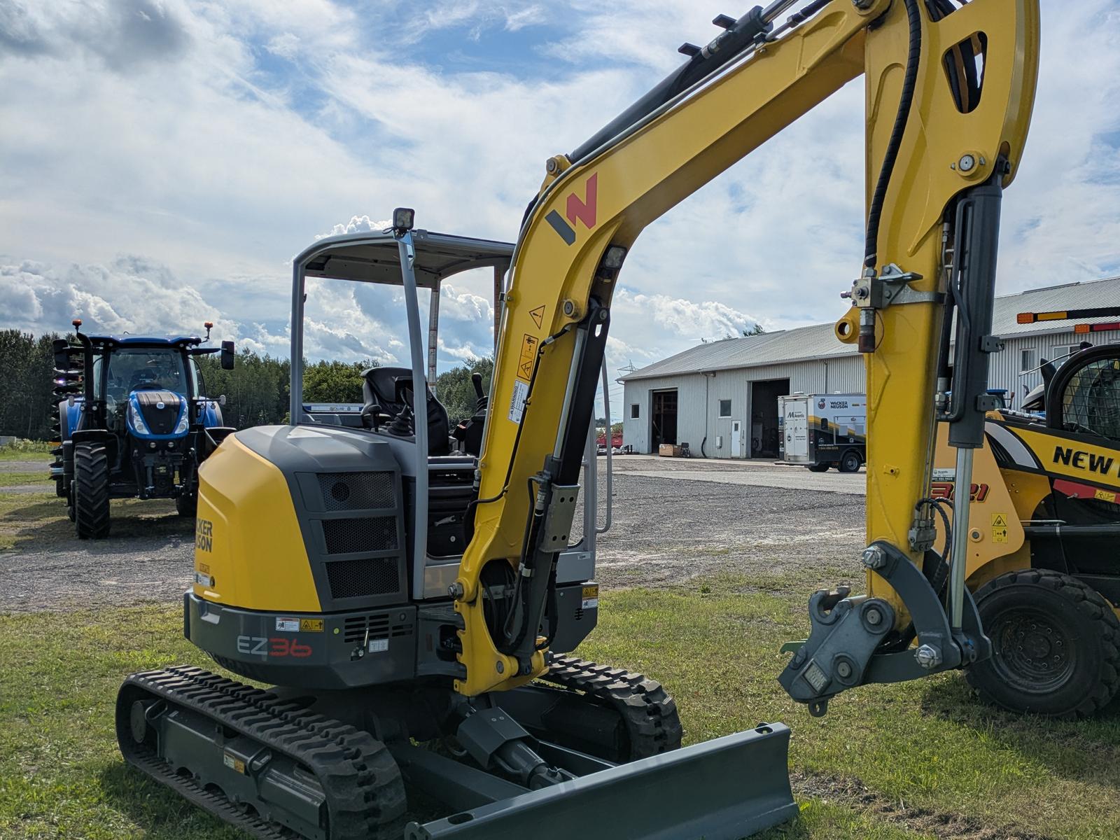 Wacker Neuson EZ36 vu de côté, bras articulé relevé, bâtiments en arrière-plan