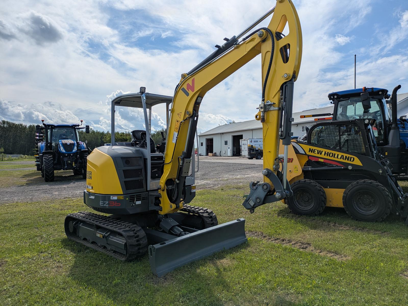 Wacker Neuson EZ36 vu de côté, bras articulé relevé, godet à l'avant, autres machines en arrière-plan