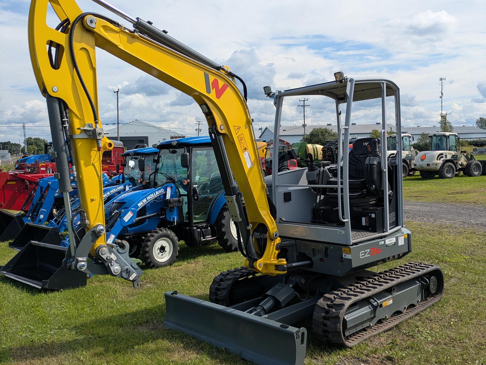 Wacker Neuson EZ36 vu de trois quarts avant, bras étendu, camion et tracteur en arrière-plan