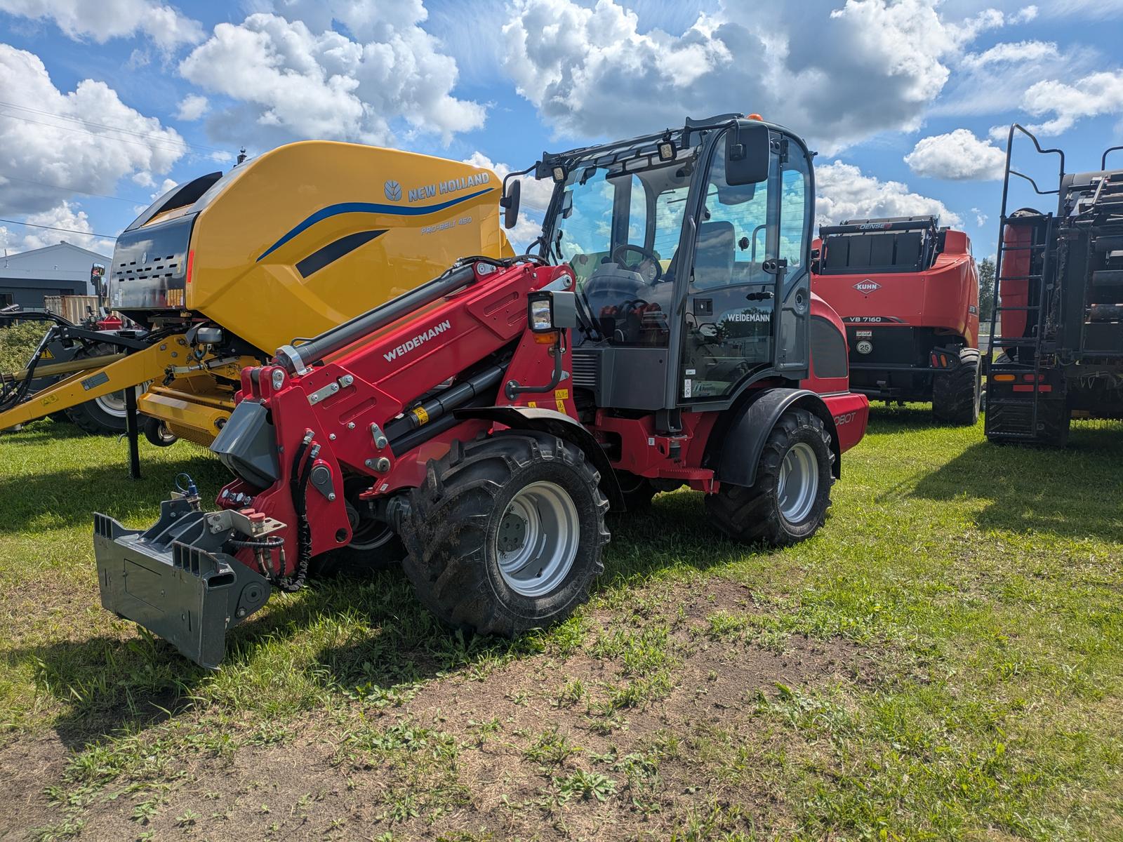 Weidemann 2080T vu de trois quarts avant avec une enrouleuse à foin jaune attelée à l'avant