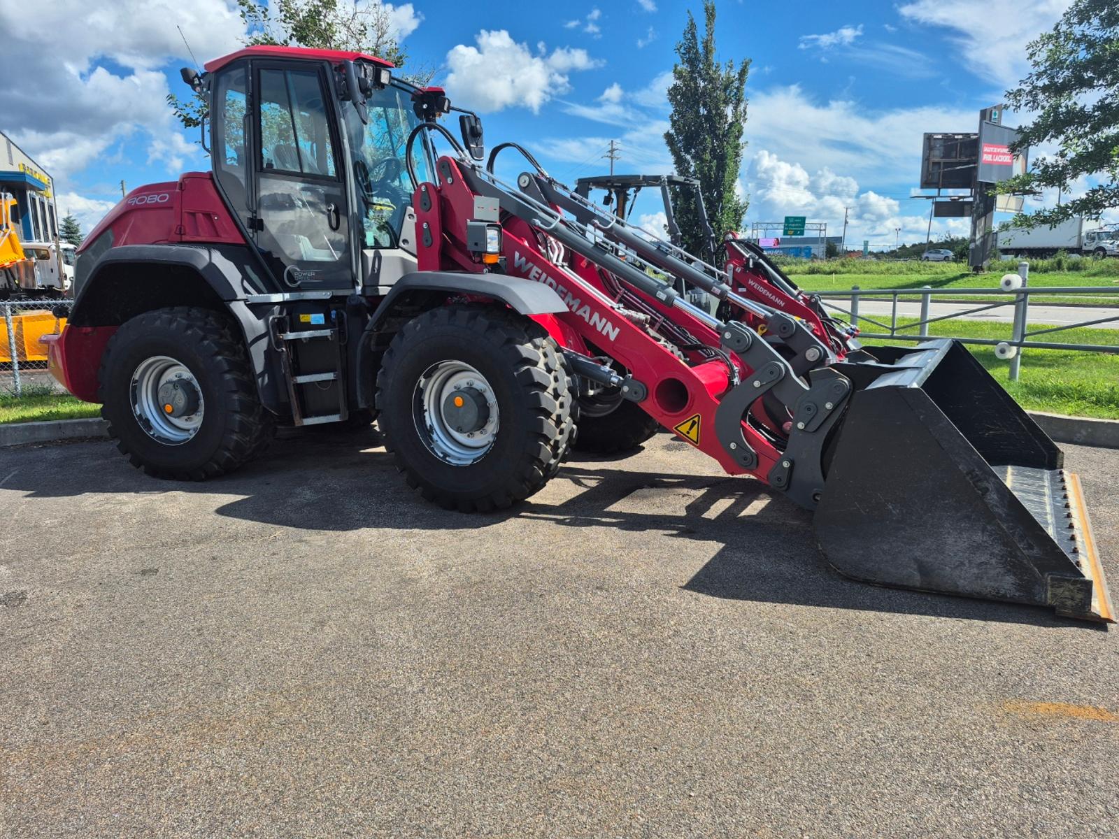 Weidemann 9080 vu de trois quarts avant-gauche, godet abaissé, enseigne routière en arrière-plan