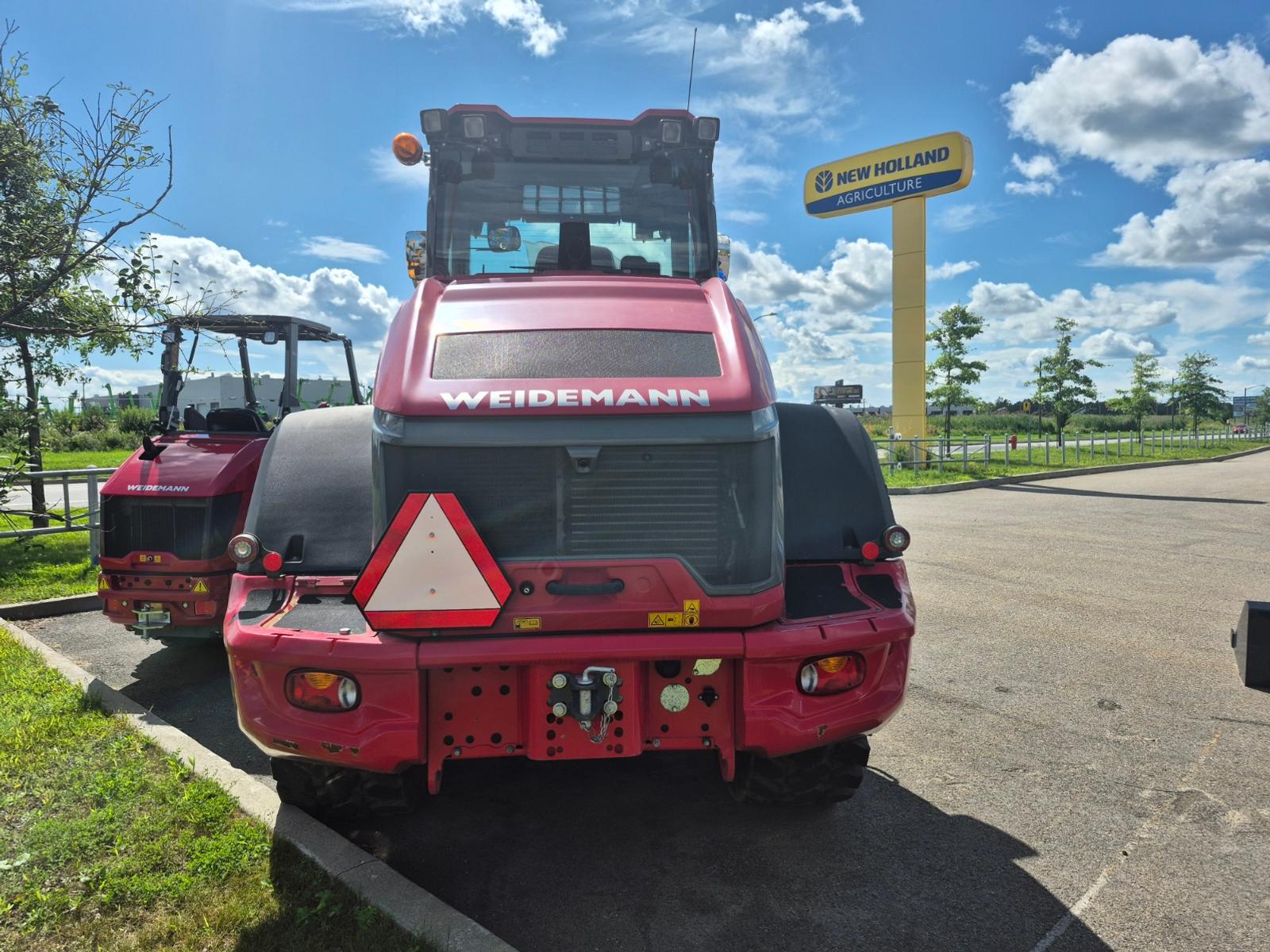 Weidemann 9080 vu de l'arrière, inscription Weidemann visible, enseigne d'un concurrent en arrière-plan