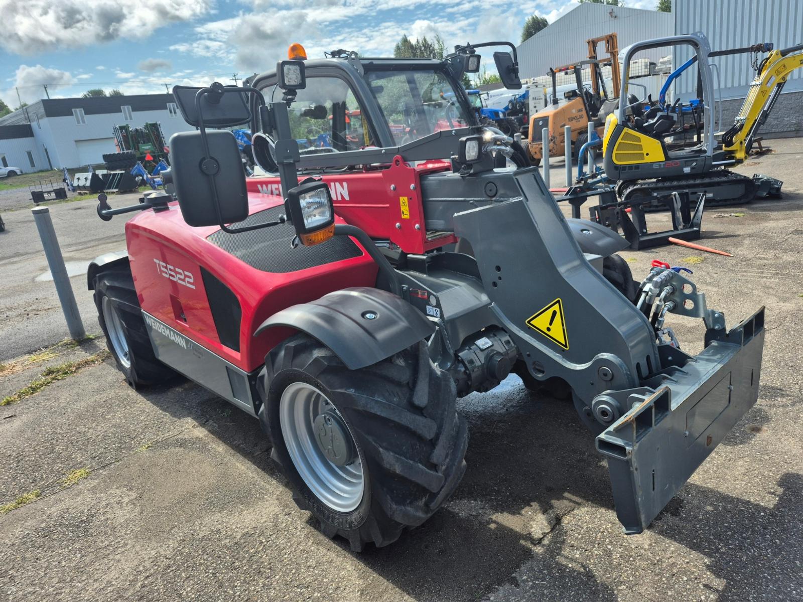 Weidemann T5522 vu de trois quarts avant-droit, carrosserie rouge et noire, autres tracteurs en arrière-plan