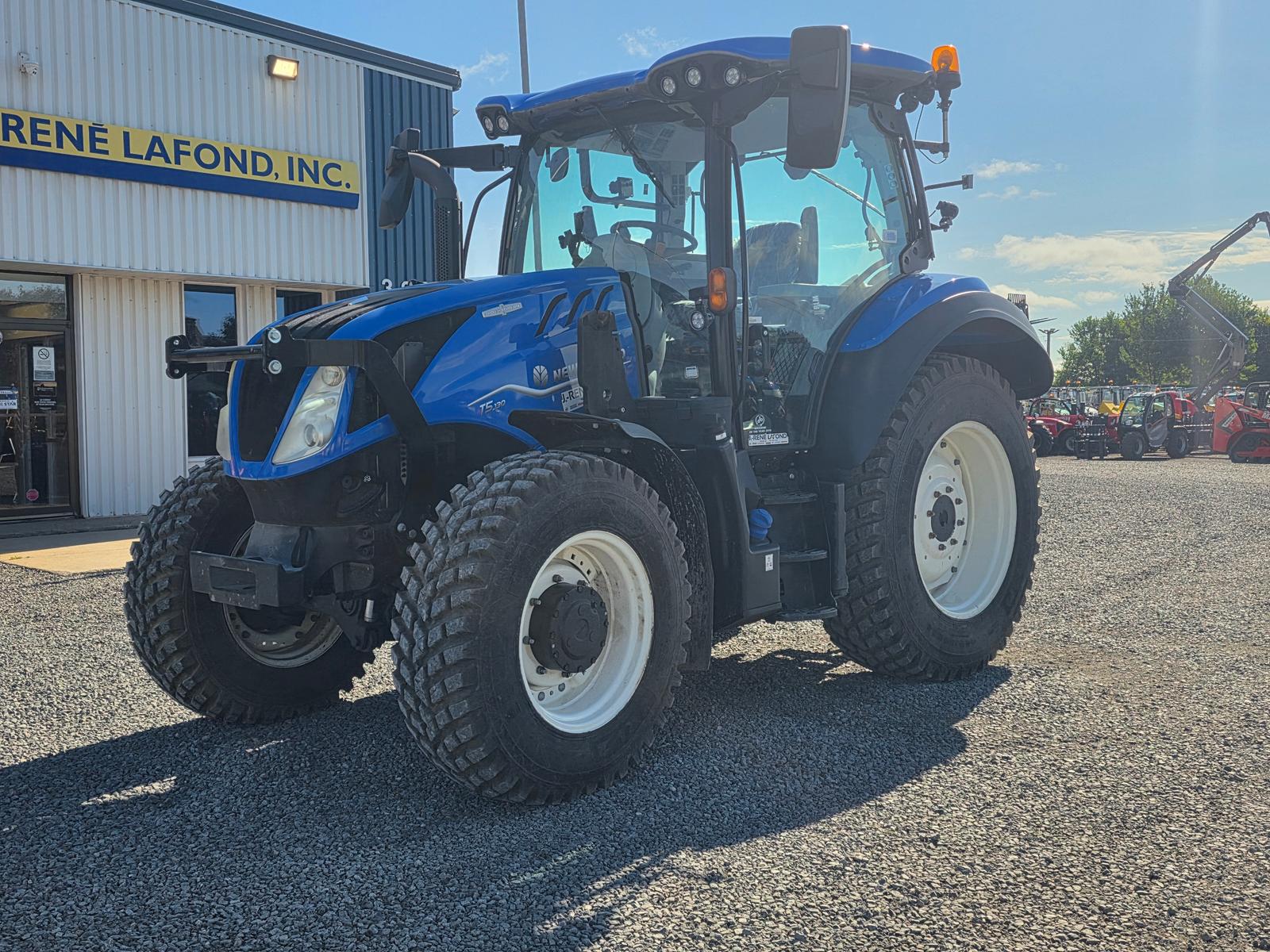 New Holland T5 vu de trois quarts avant-gauche, devanture du concessionnaire en arrière-plan
