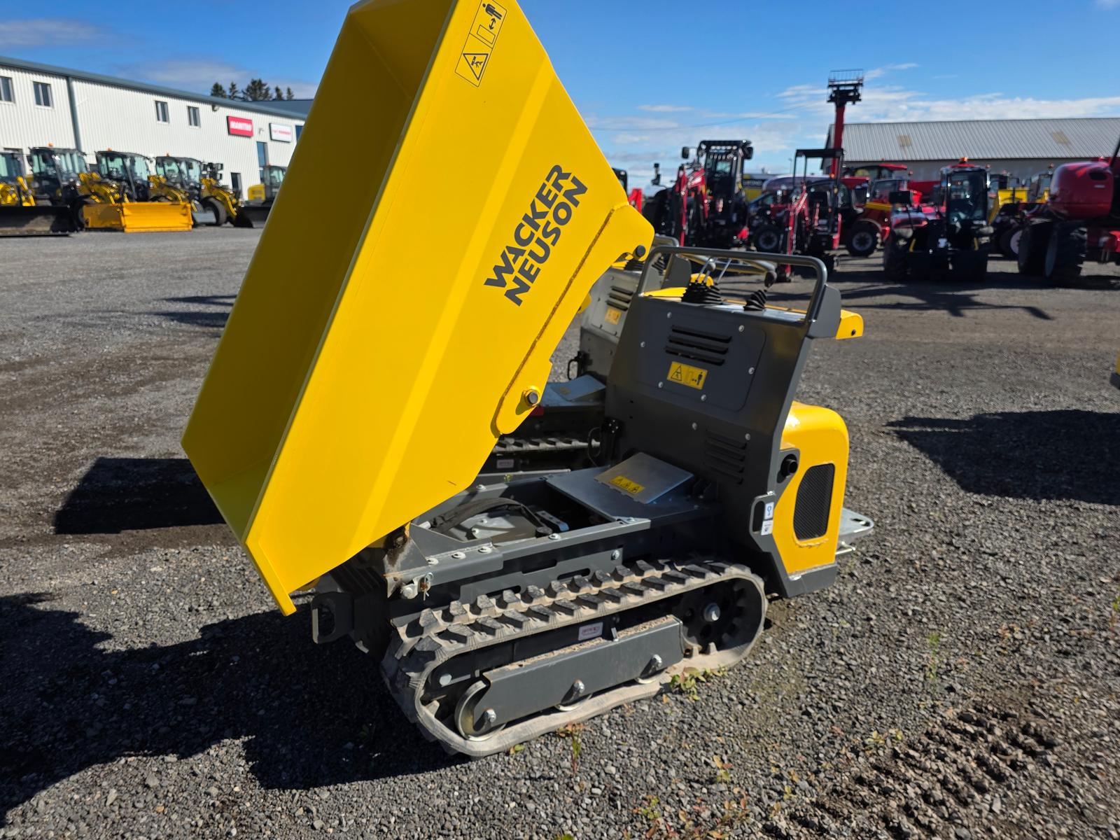 Wacker Neuson DT08 vu de trois quarts arrière, benne levée, autre machinerie et enseigne Wacker Neuson en arrière-plan