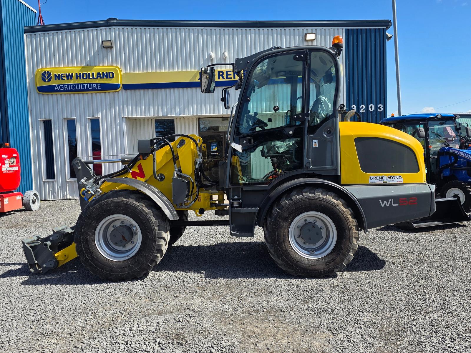 Wacker Neuson WL52 vu de côté, godet à l'avant, enseigne New Holland Agriculture et bâtiment du concessionnaire en arrière-plan