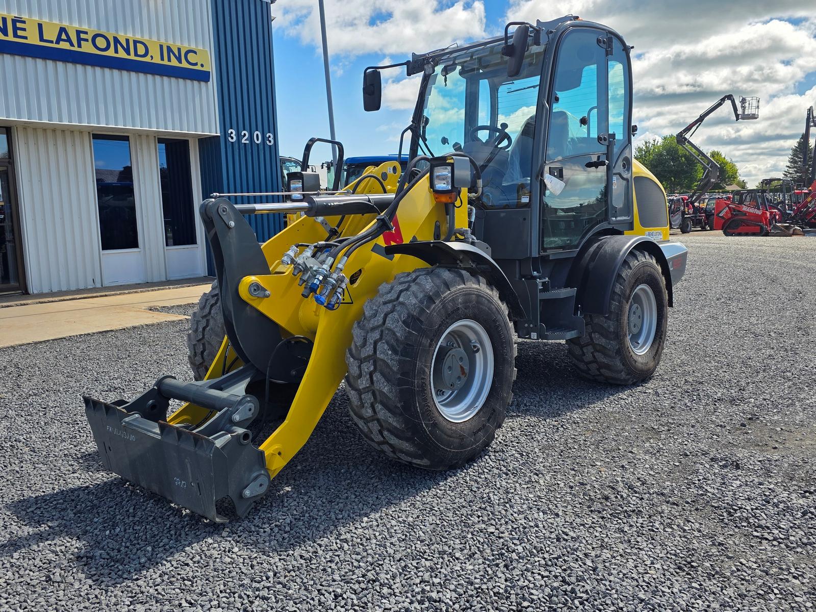 Wacker Neuson WL52 vu de trois quarts arrière-gauche, godet basculé vers l'avant, autres machines en arrière-plan