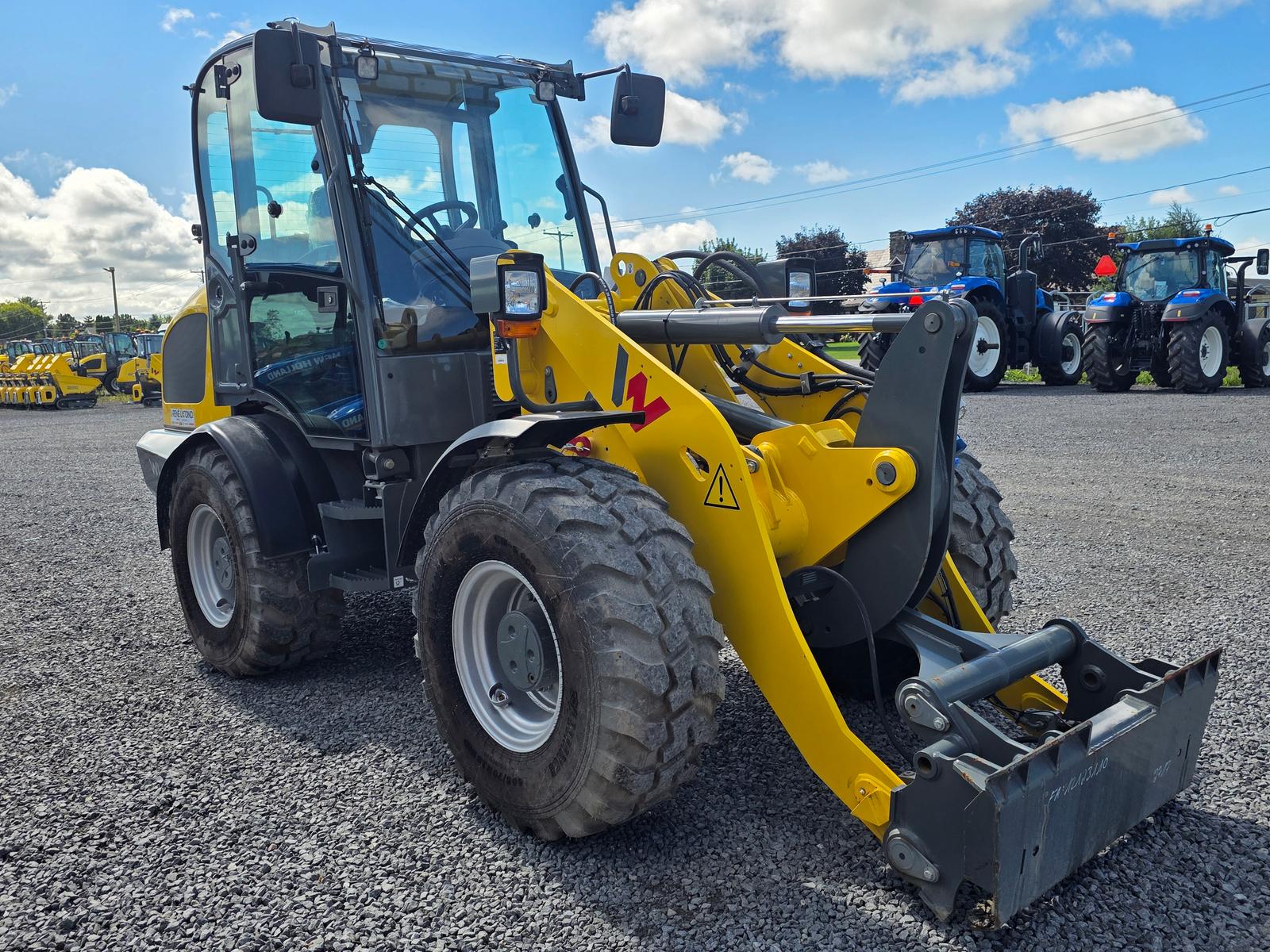 Wacker Neuson WL52 vu de trois quarts avant-droit, tracteurs New Holland stationnés en arrière-plan