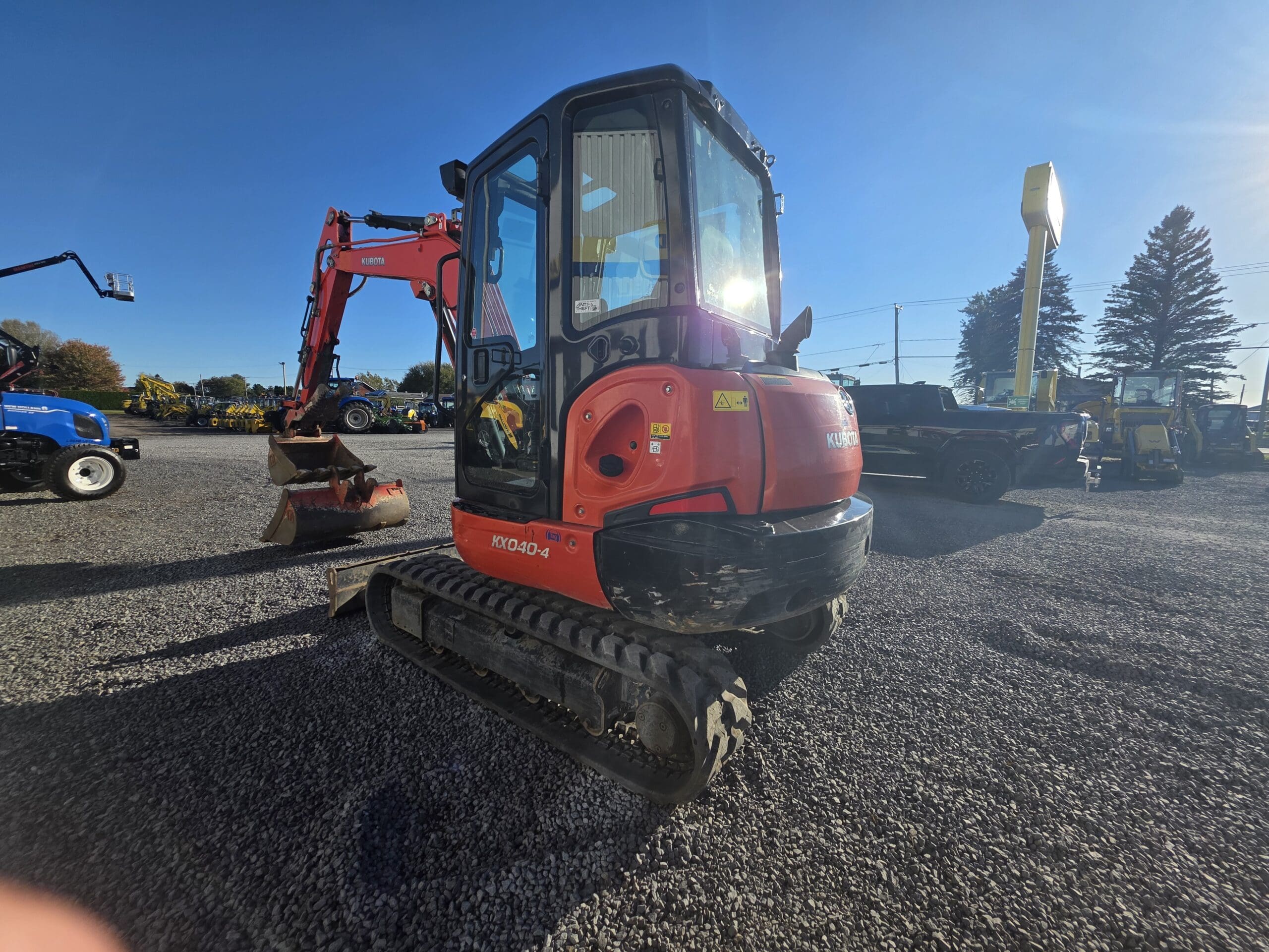 Une petite pelleteuse Kubota KX040-4 rouge, garée sur un terrain en gravier.