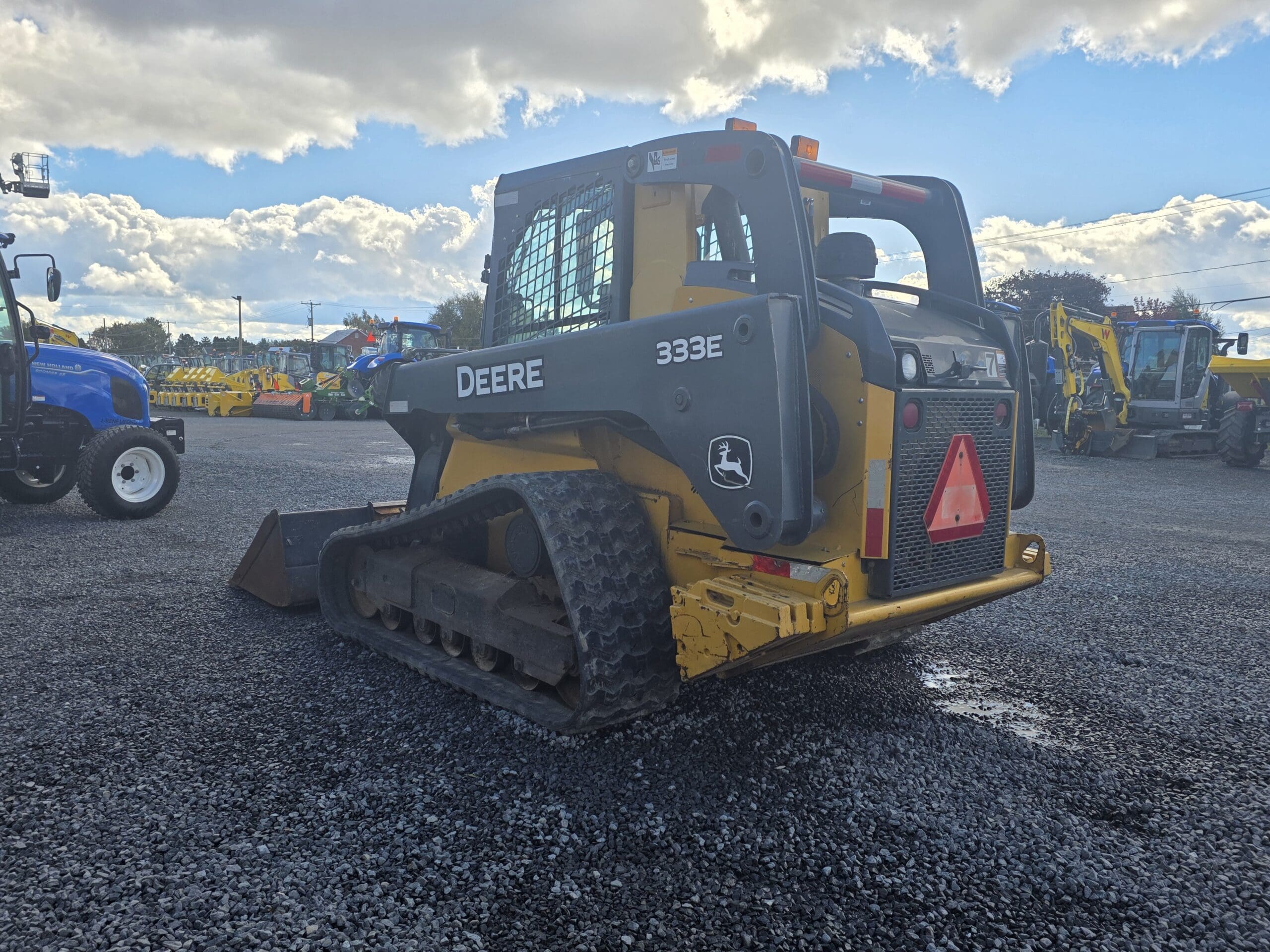 Une chargeuse compacte sur chenilles John Deere 333E garée sur un terrain en gravier.