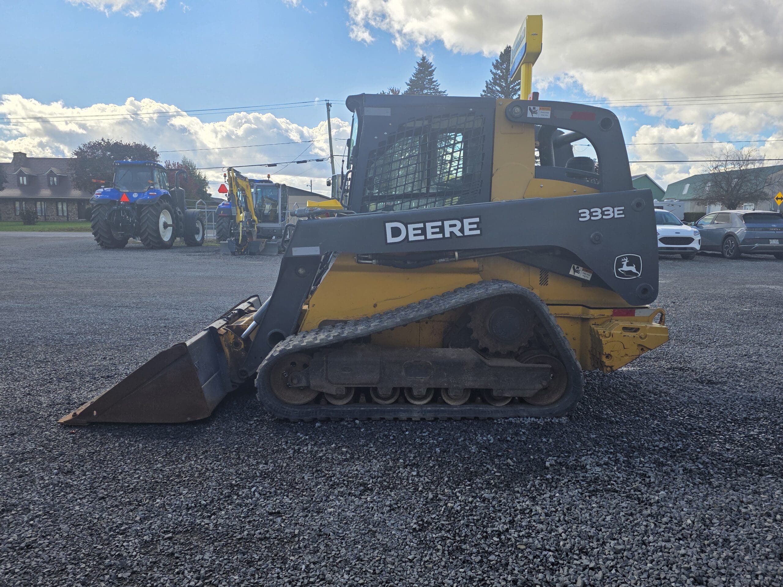 Une chargeuse compacte sur chenilles John Deere 333E de couleur jaune est garée sur un terrain en gravier.