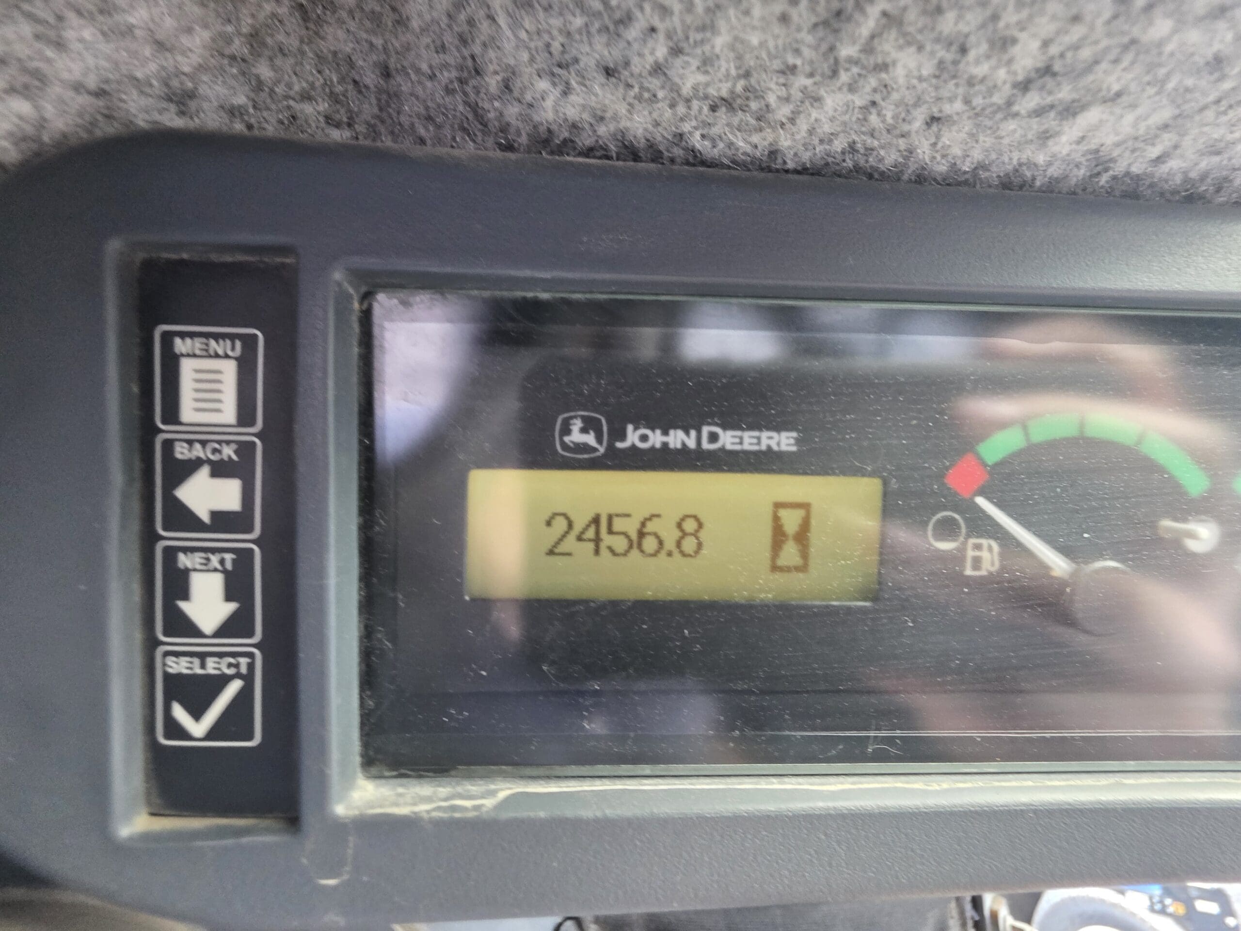 Écran de l'équipement John Deere affichant 2 456,8 heures de fonctionnement du moteur, avec des boutons de navigation dans les menus à gauche et une jauge de carburant à droite.