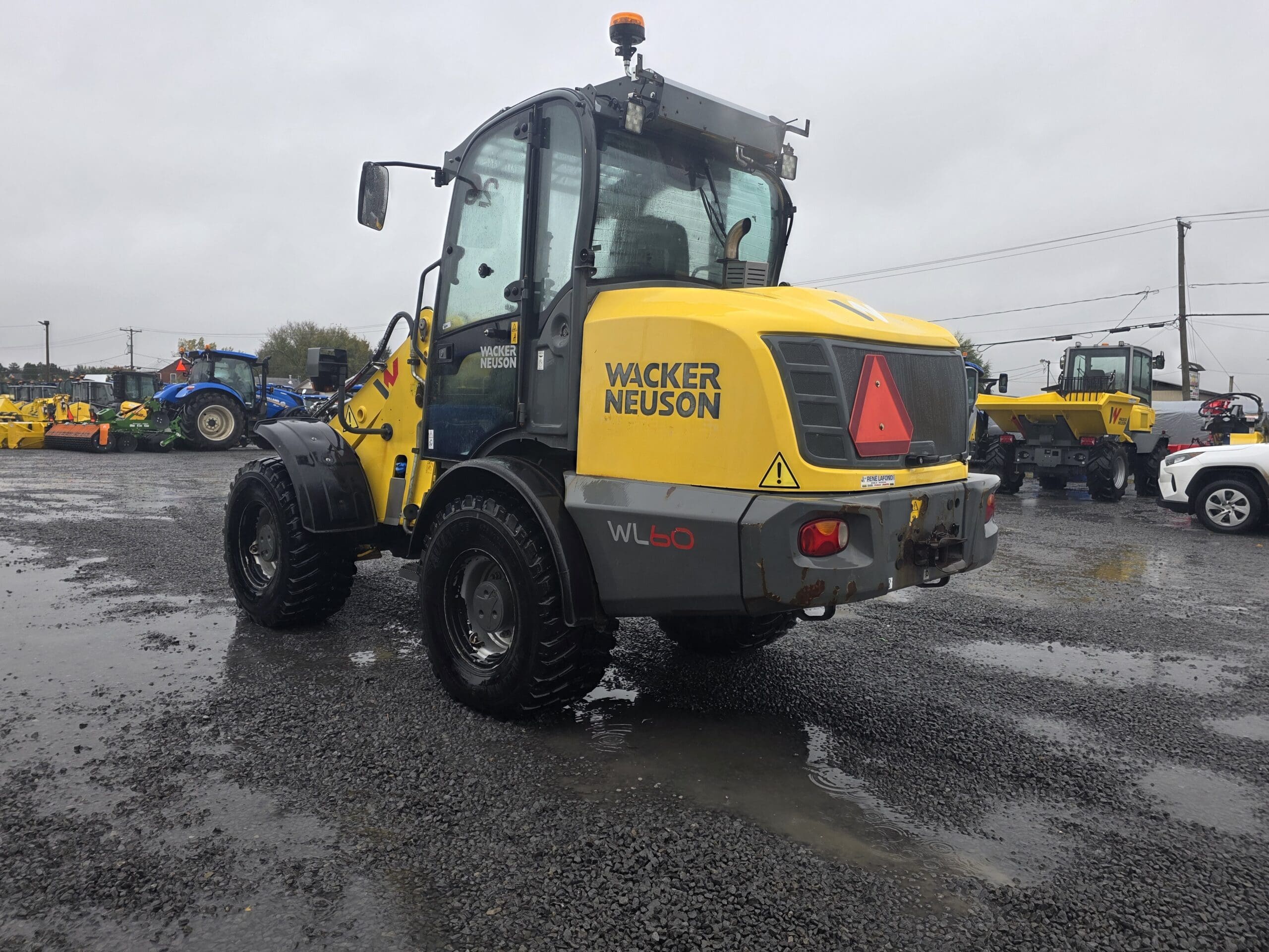 Une chargeuse sur pneus Wacker Neuson WL60 jaune, garée sur un terrain en gravier.