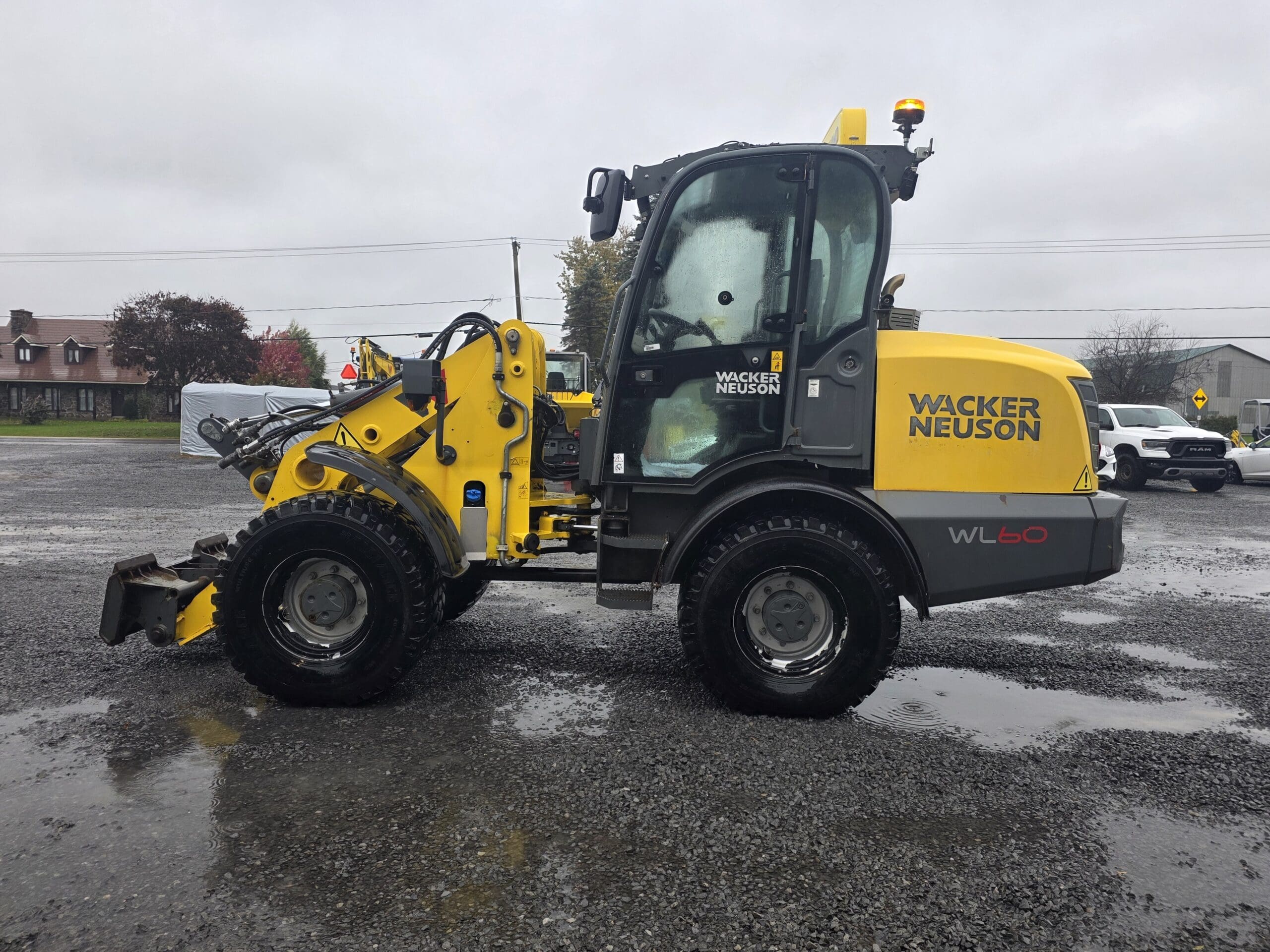Une chargeuse sur pneus Wacker Neuson WL60 jaune, garée sur un terrain en gravier mouillé.